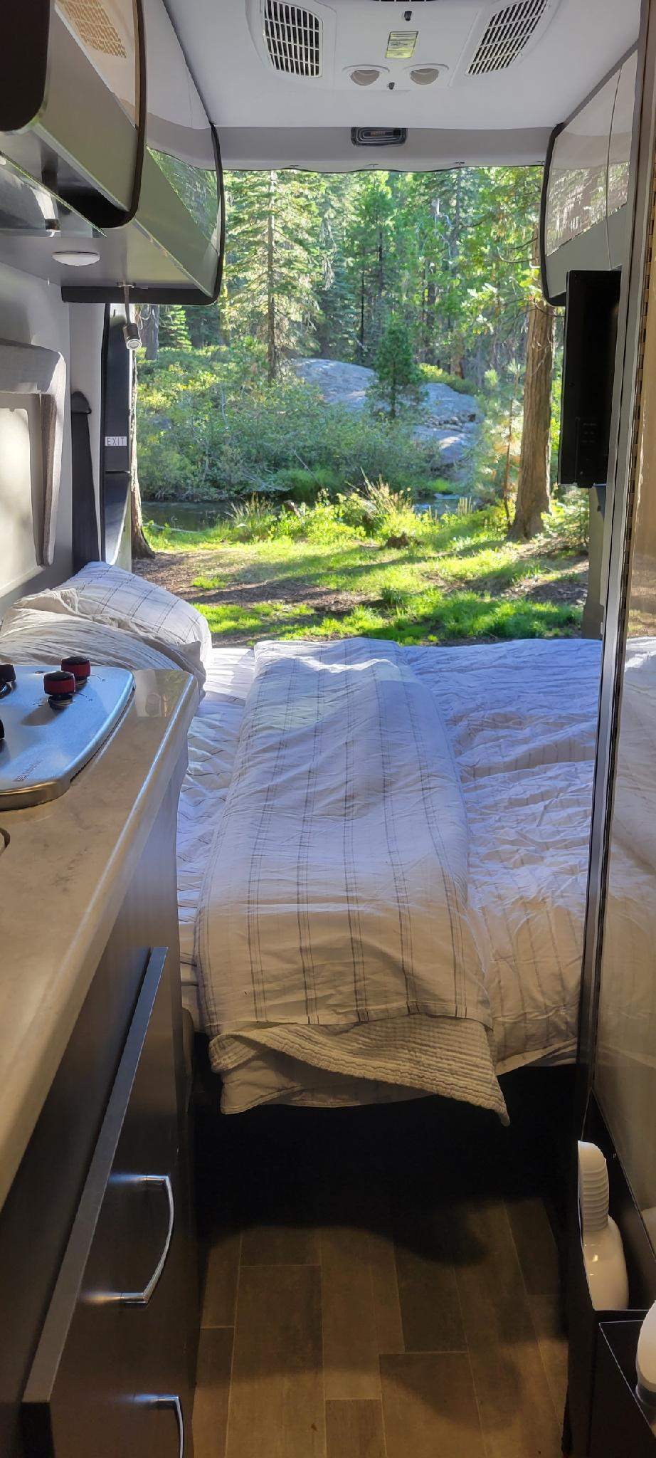 Cozy rv rental interior with a bed looking out onto a stunning forest and stream view. Perfect for nature lovers.. Thor Synergy 2022