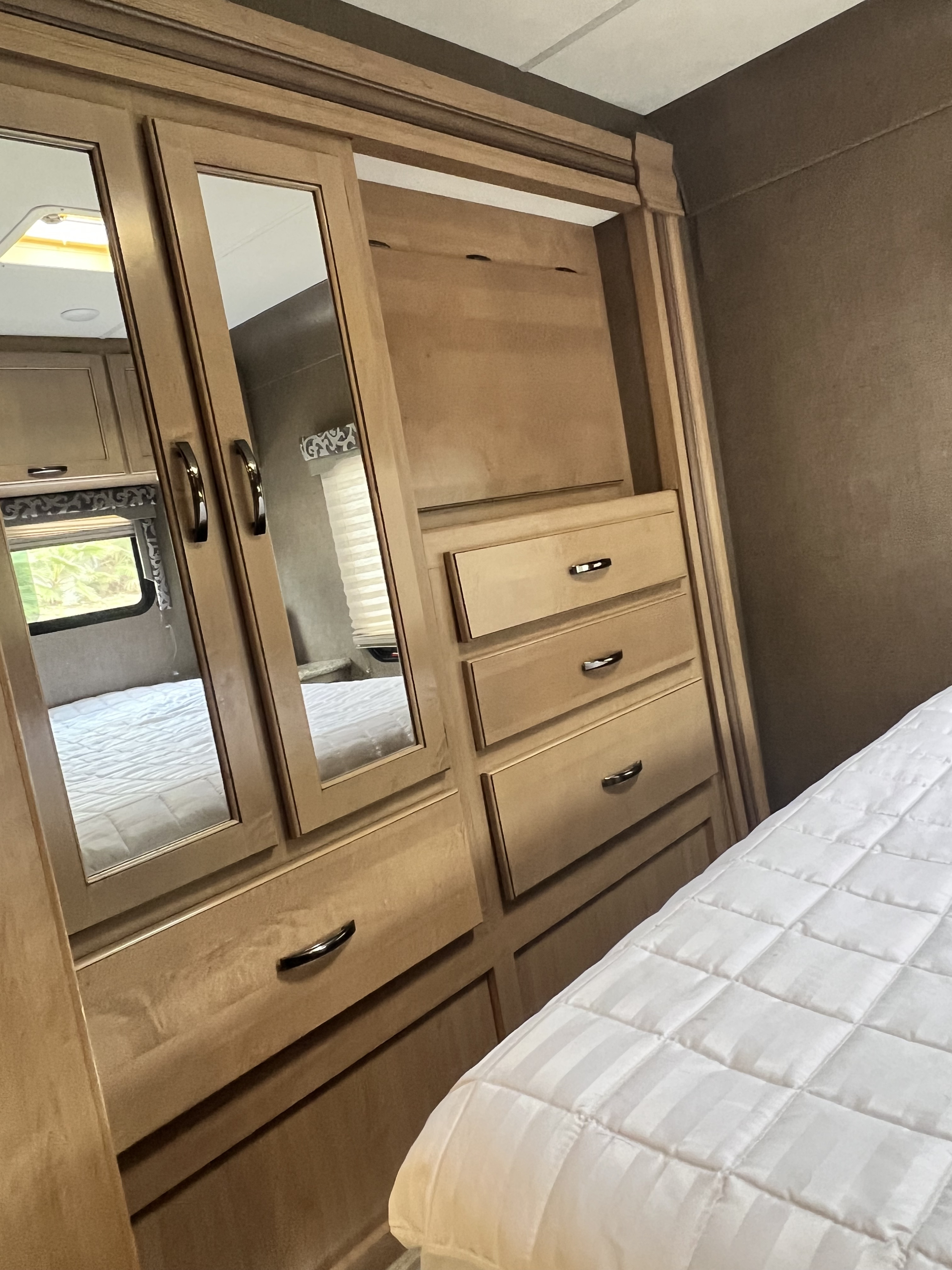 Step inside this RV rental's compact bedroom, featuring a mirrored wardrobe, dresser with drawers, and a white quilted bed.. Thor Four Winds 2017
