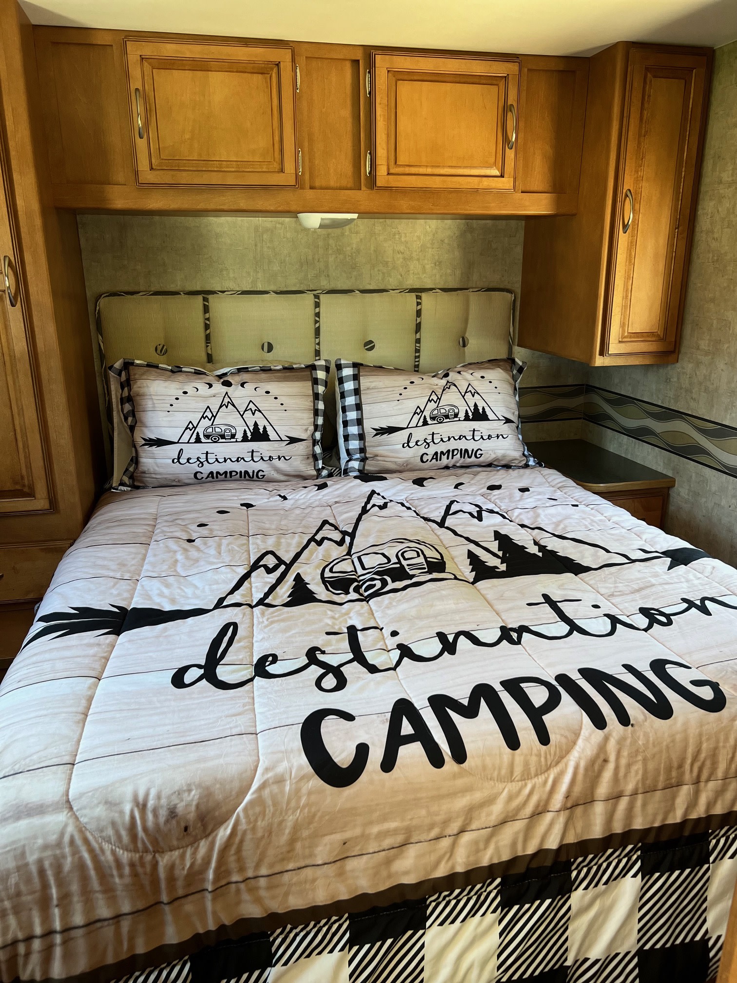 This RV rental bedroom features a comfy bed with "destination CAMPING" comforter & pillows, surrounded by warm wood cabinetry.. Winnebago Minnie Winnie 2015