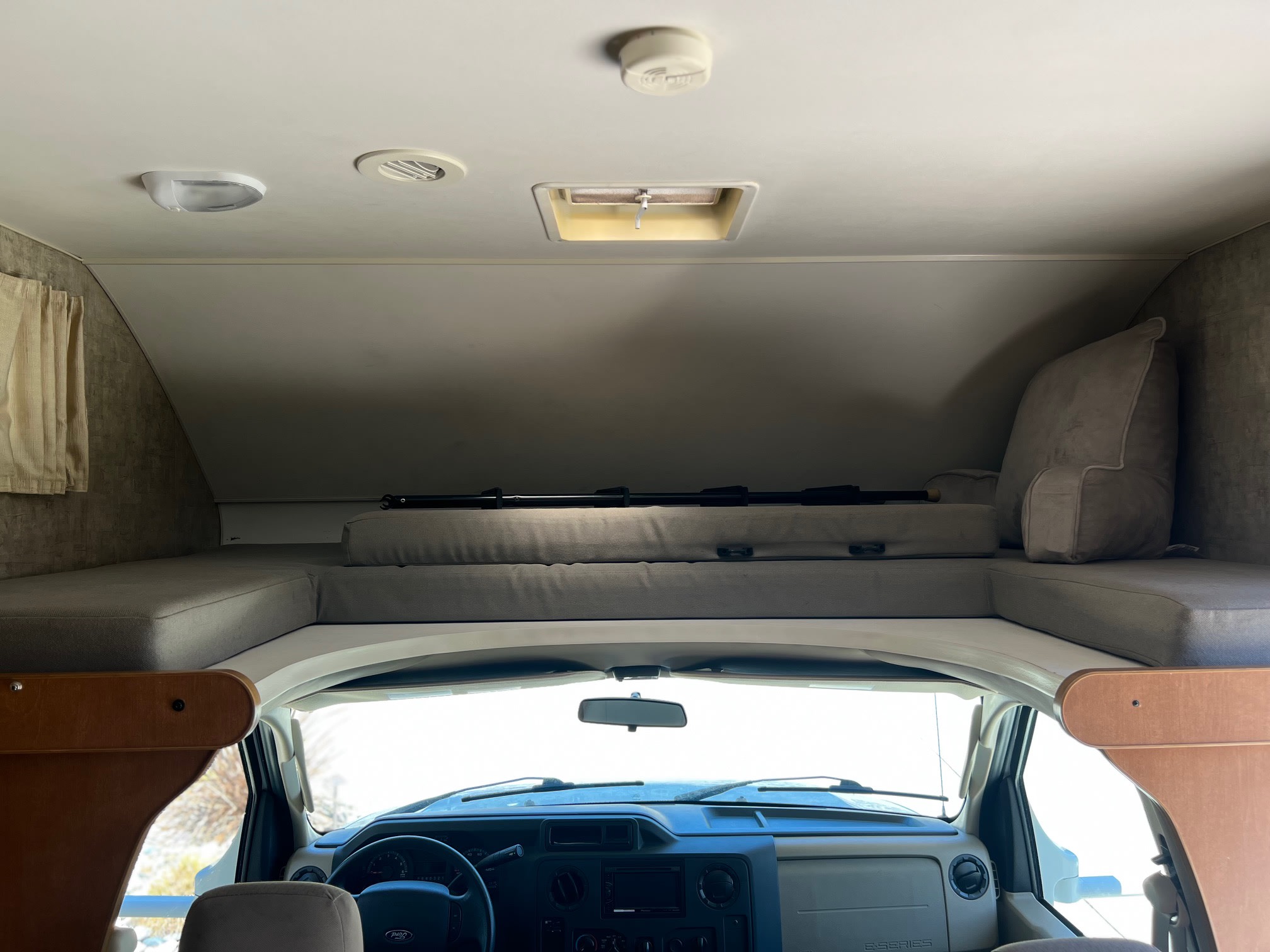 Inside an **RV rental**: the comfy cab-over bunk sleeping area is visible above the driver's dashboard and steering wheel.. Winnebago Minnie Winnie 2015