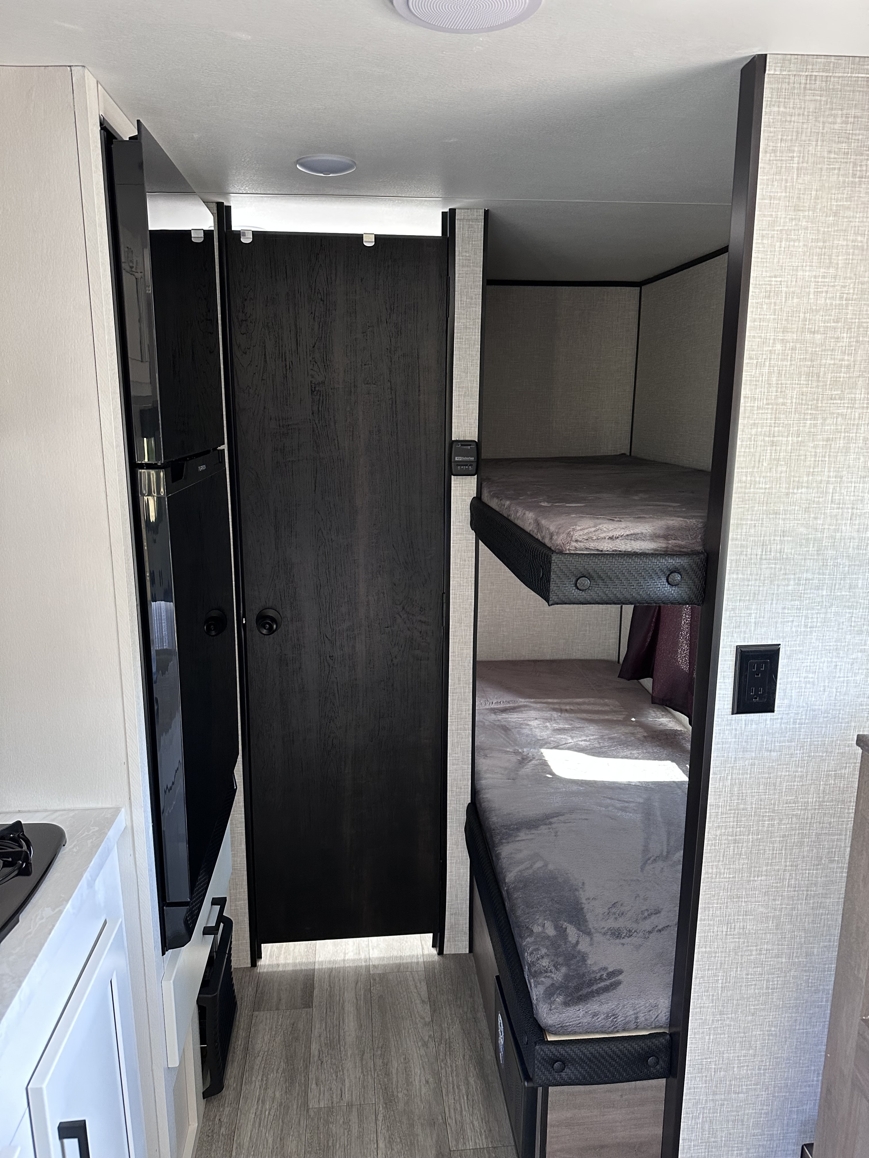 RV rental interior with a compact kitchen and black fridge, dark wood door, and two comfortable bunk beds.. Jayco Jay Flight SLX Baja Edition 2024