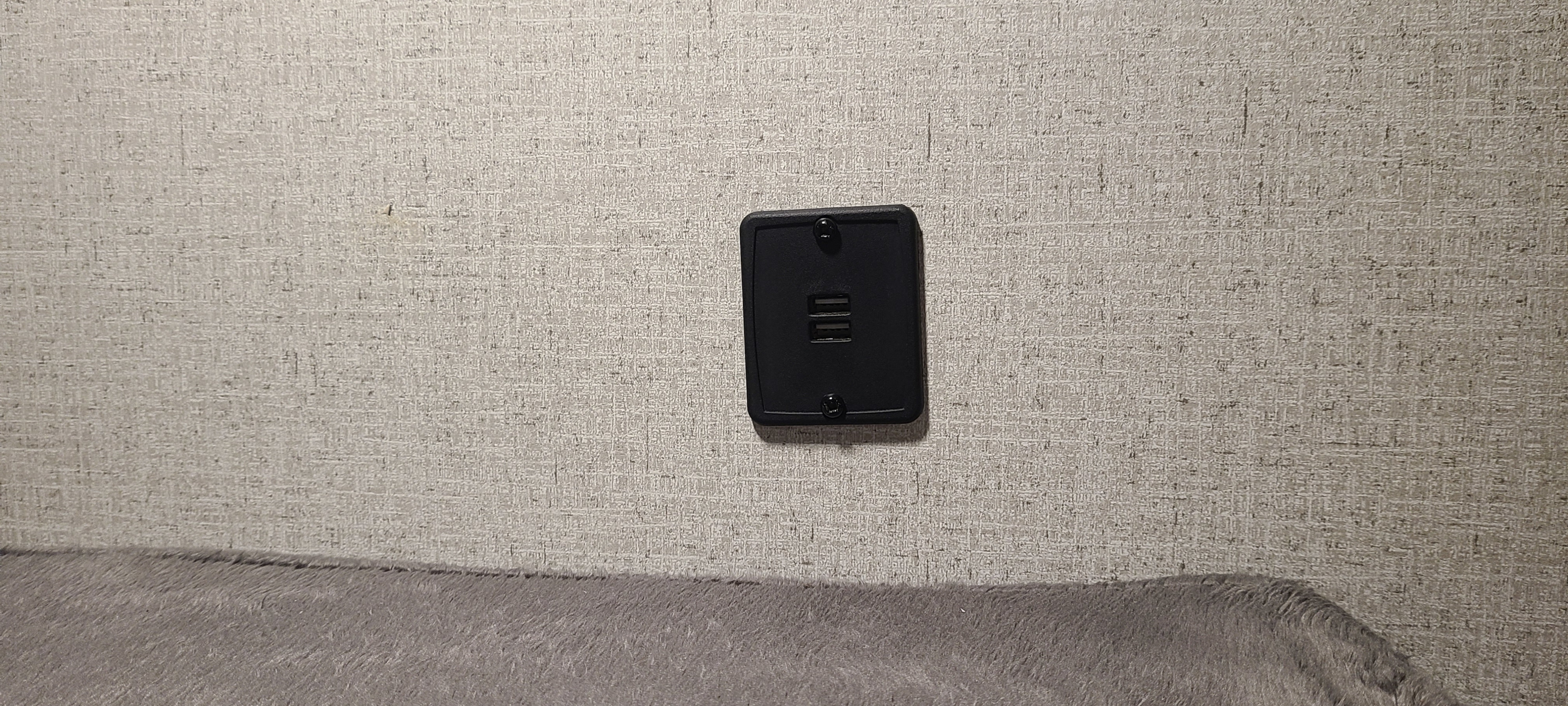 An RV rental interior features a black wall-mounted USB charging port on a textured wall, above a grey upholstered surface.. Coleman Lantern 2021