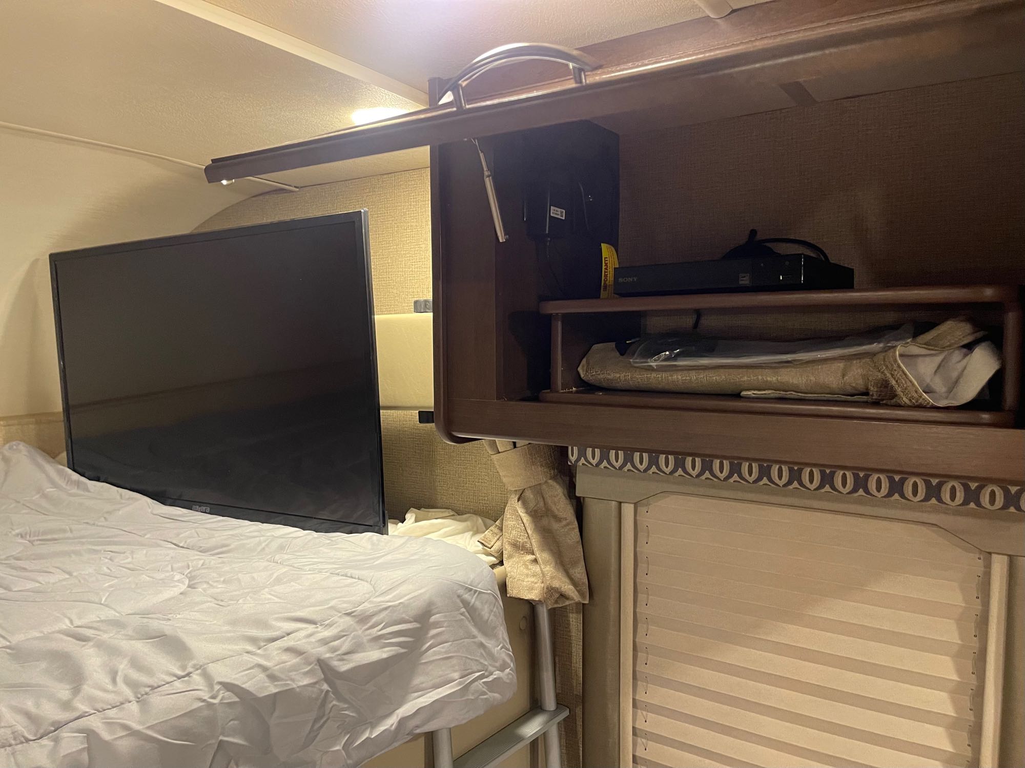 This rv rental interior features a cozy bunk with TV, overhead console, and ladder, plus window blinds for privacy.. Thor Freedom Elite 2018