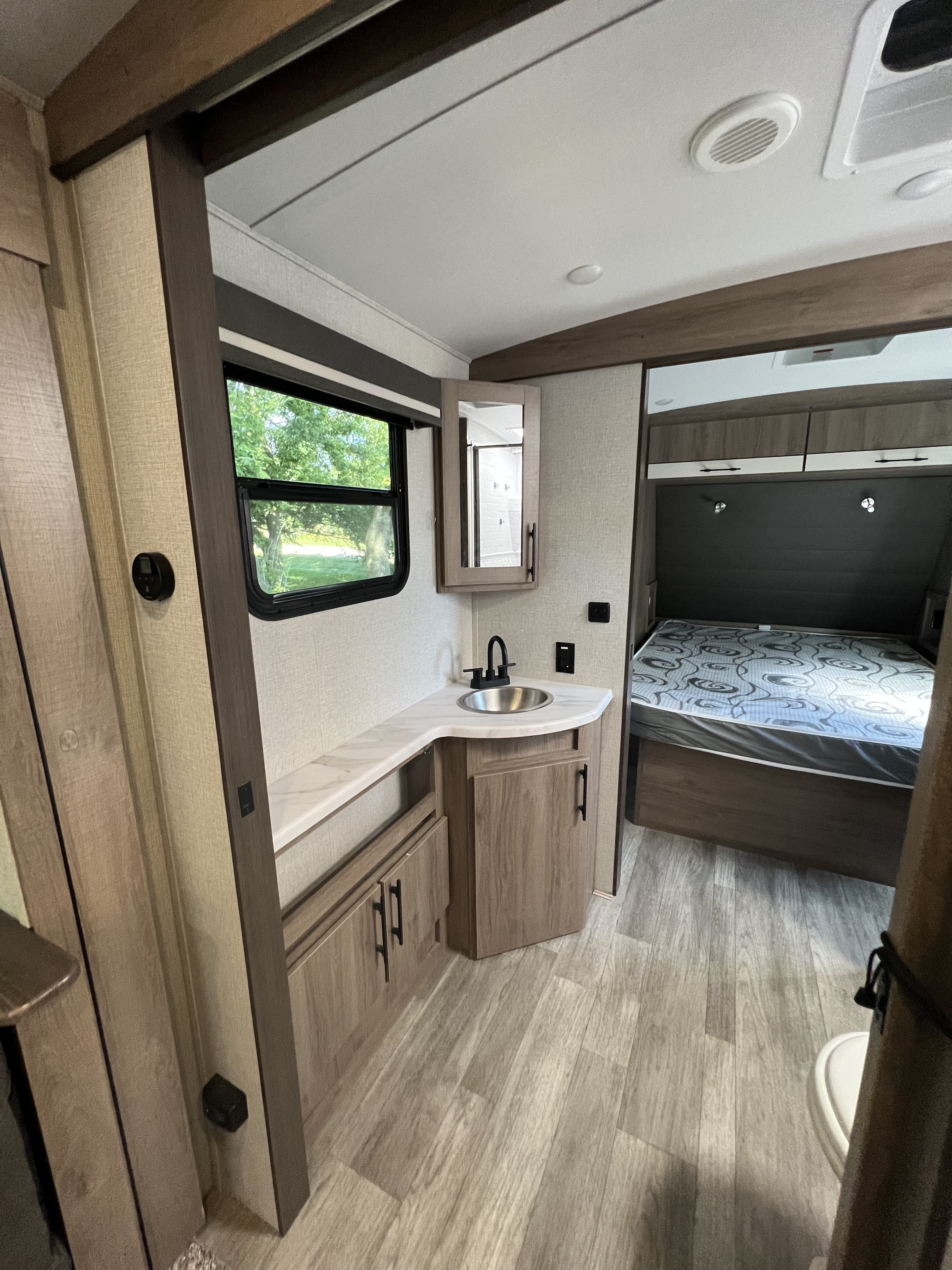 RV rental interior: practical vanity with sink, mirror, storage cabinets, and a comfortable bed. Bright, modern living space for travel.. Grand Design Imagine 2023