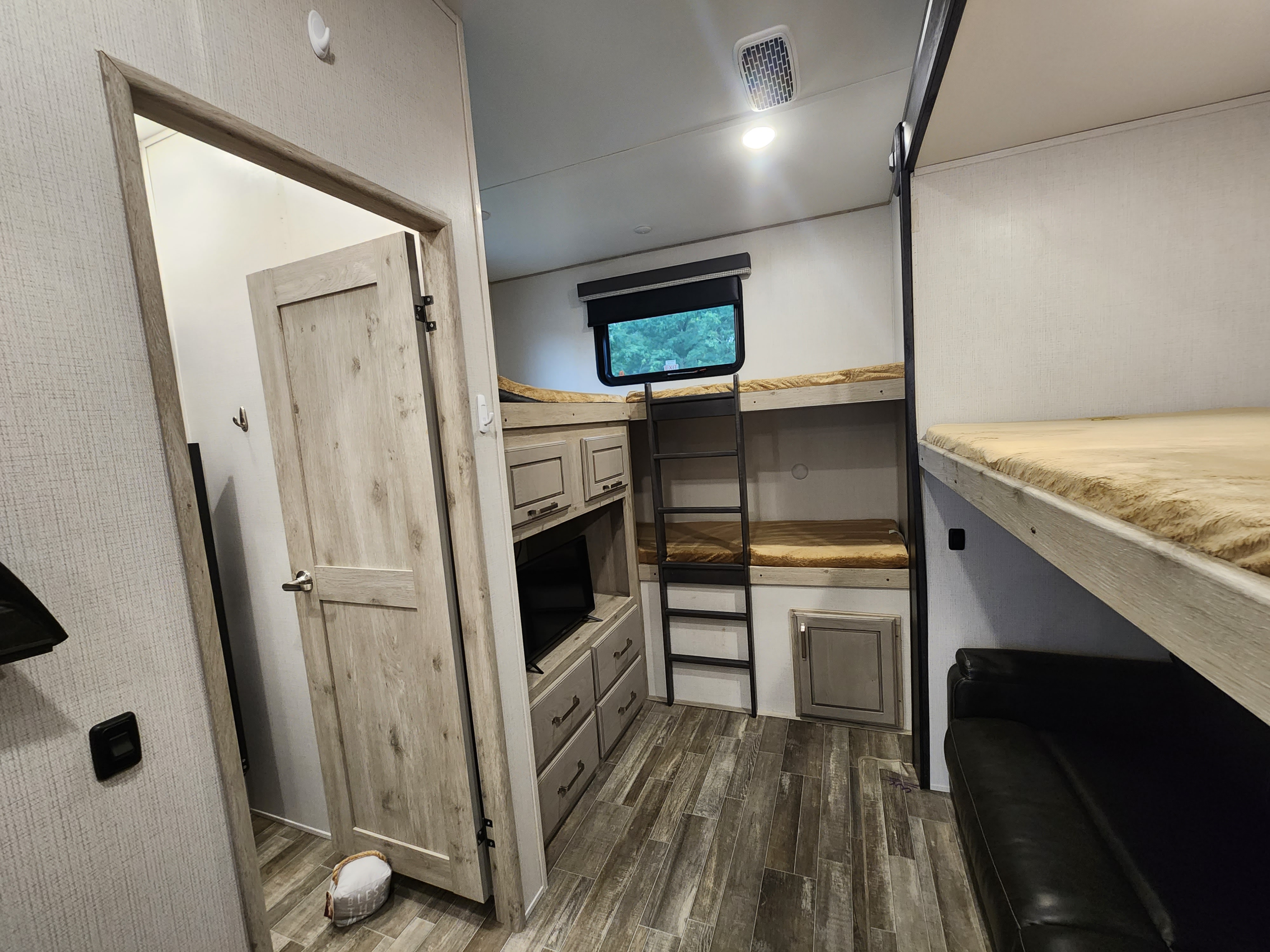 RV rental bunk room: features multiple beds, built-in entertainment center with TV, storage, and a black sofa.. Keystone Avalanche 2021