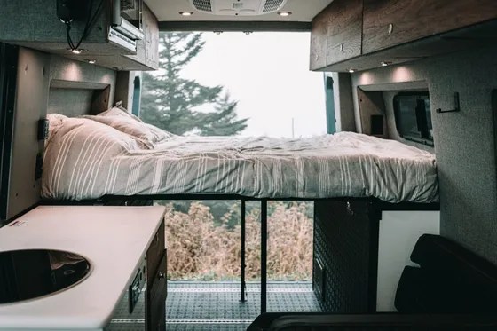 Inside an RV rental camper van: elevated bed, compact kitchen area, and nature views. Ideal for road trip adventures.. Storyteller Overland Storyteller Overland Class B 2022