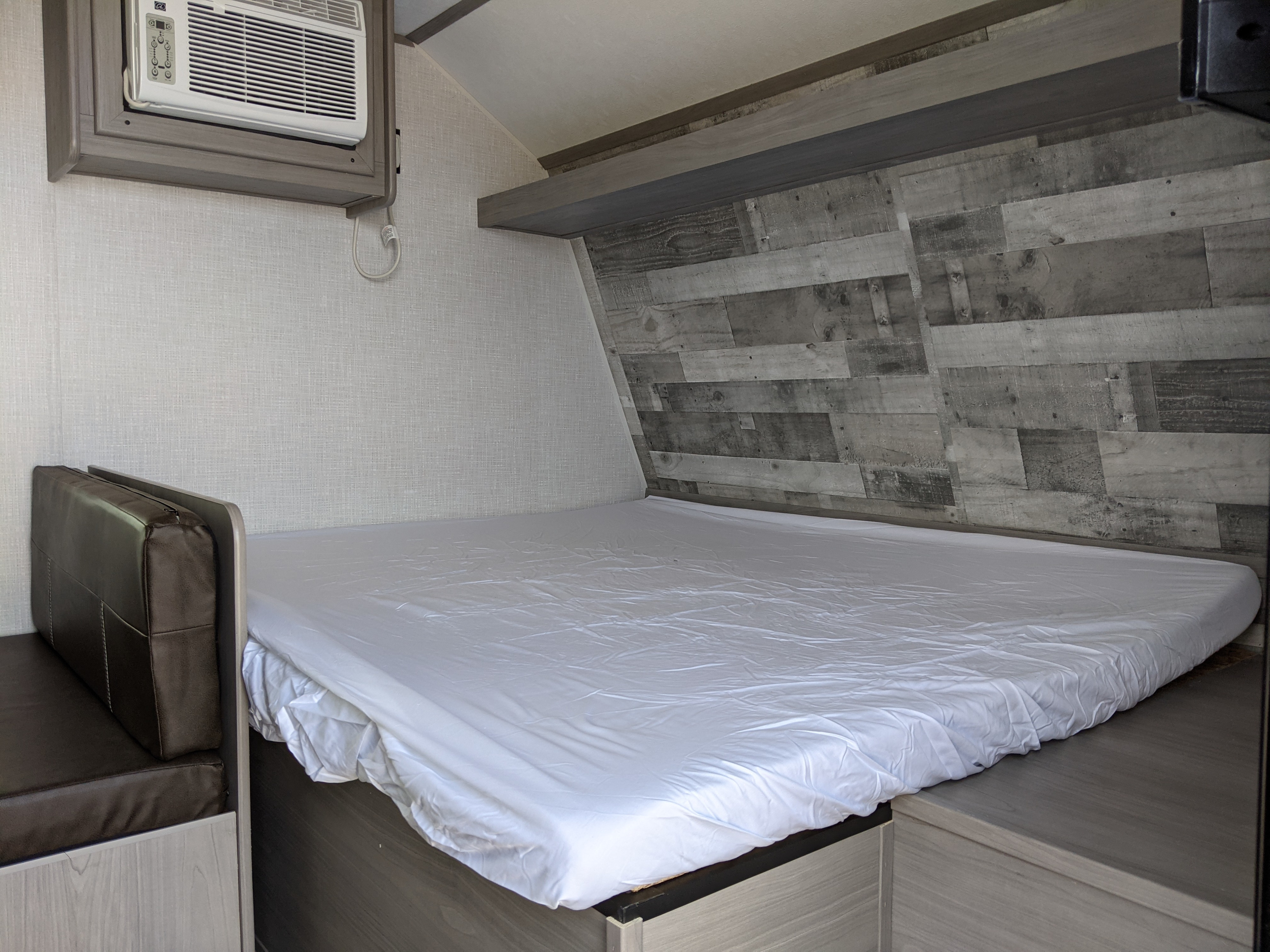 Compact RV rental bedroom with a comfy bed, AC unit, and integrated bench seating.. Dutchmen 17B 2023