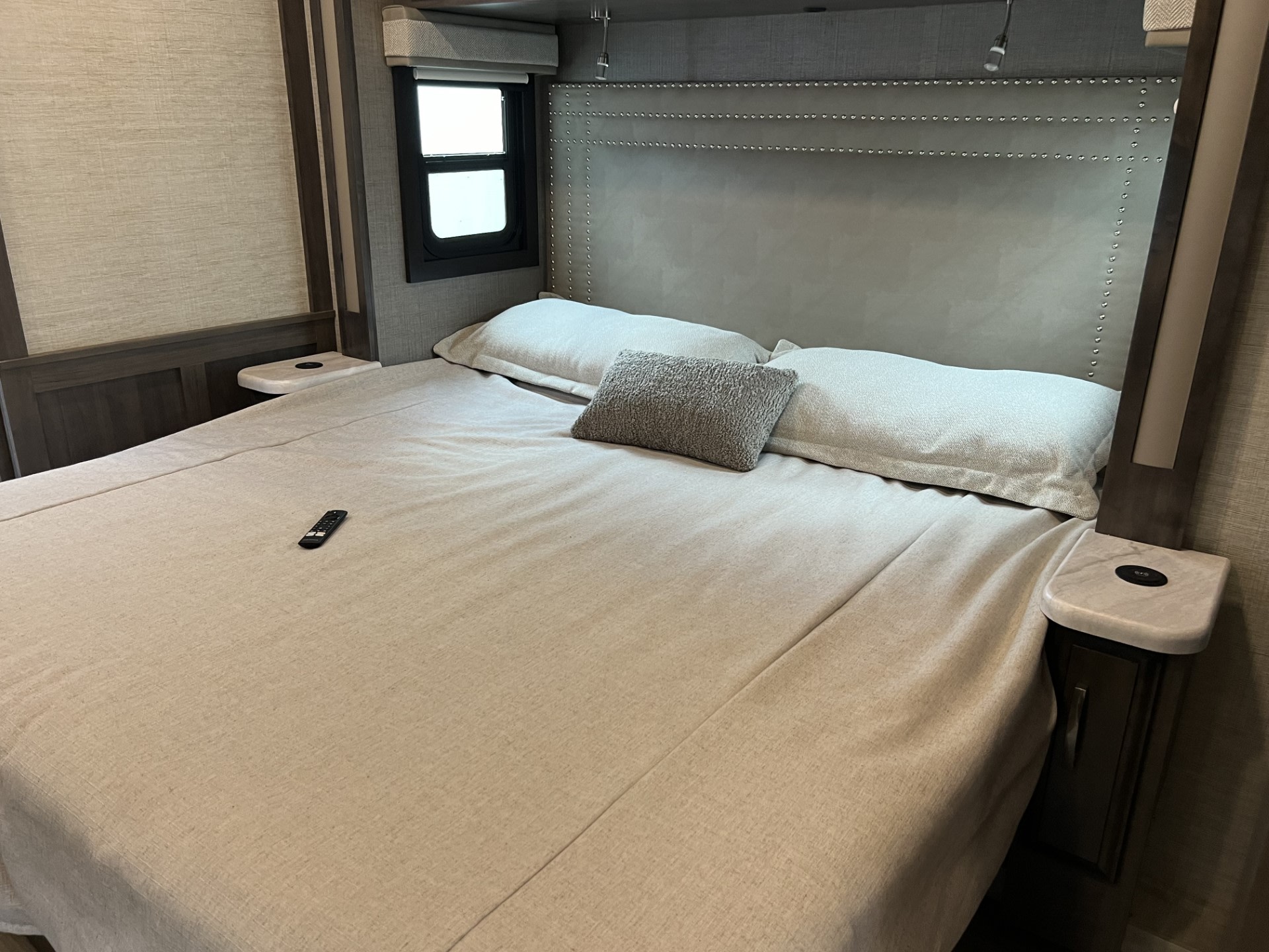 Relaxing RV rental bedroom: cozy bed with studded headboard, side tables with charging, and window for natural light.. Entegra Coach Vision XL 2023