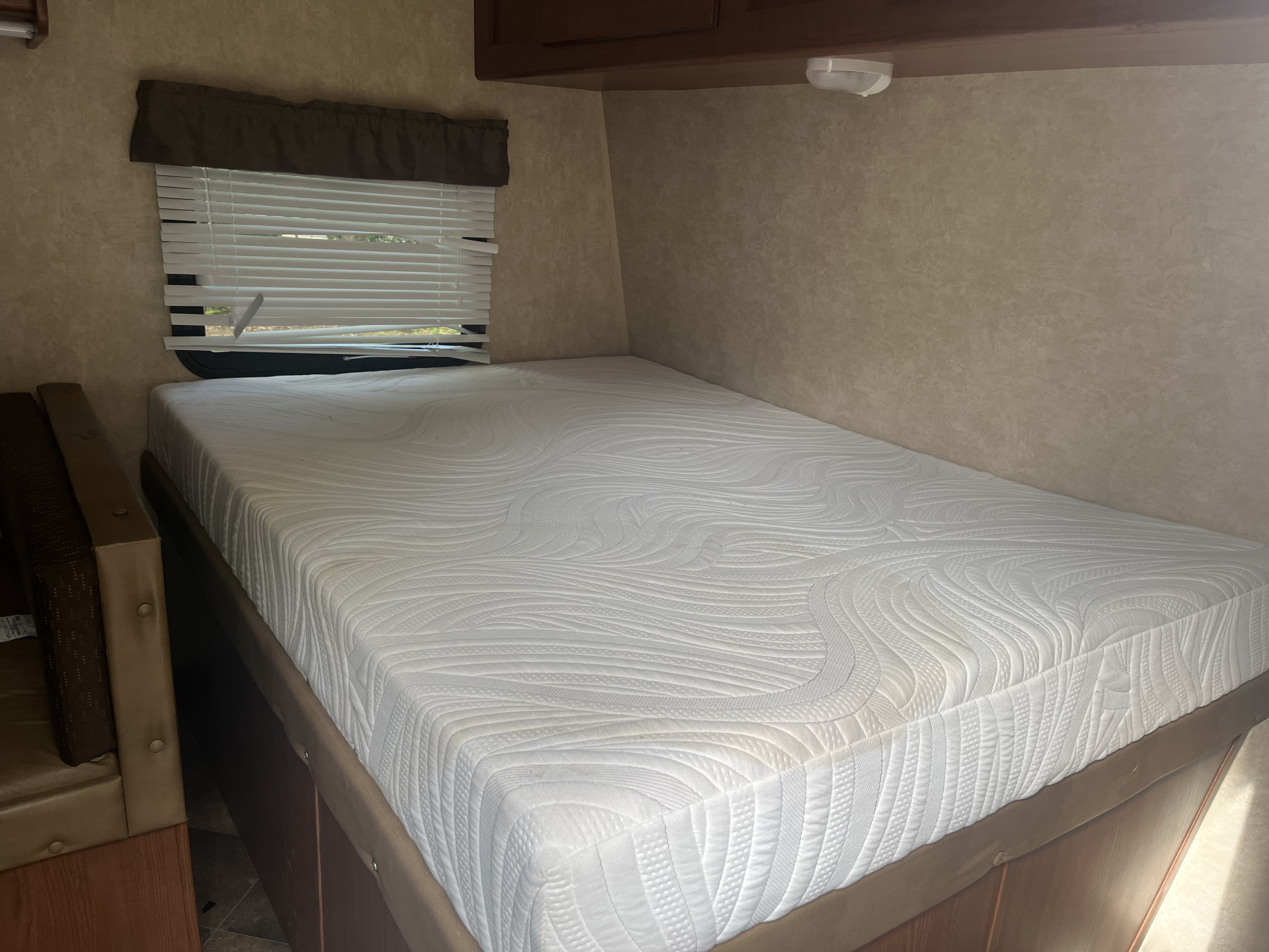 Cozy RV rental bedroom featuring a comfortable white patterned mattress, window with blinds, and compact design.. Forest River Salem Cruise Lite 2015