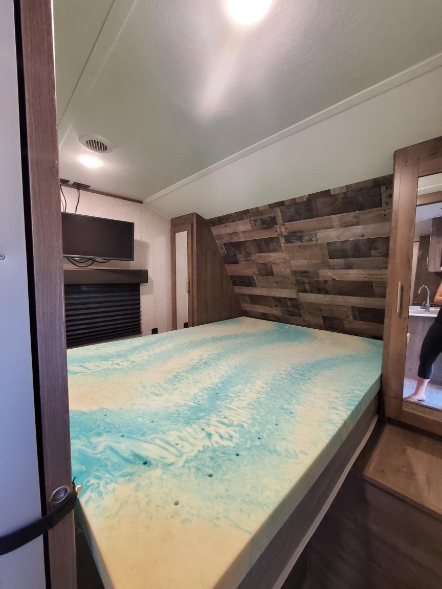 Cozy RV rental bedroom featuring a bed with a blue swirled memory foam topper, wood accent wall, and TV.. Aspen Trail LE 2021