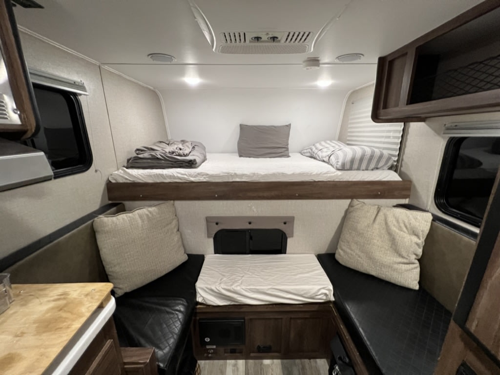 Cozy RV rental interior with elevated bunk bed, convertible dining/seating, and plush cushions.. Travel Lite 770R 2020