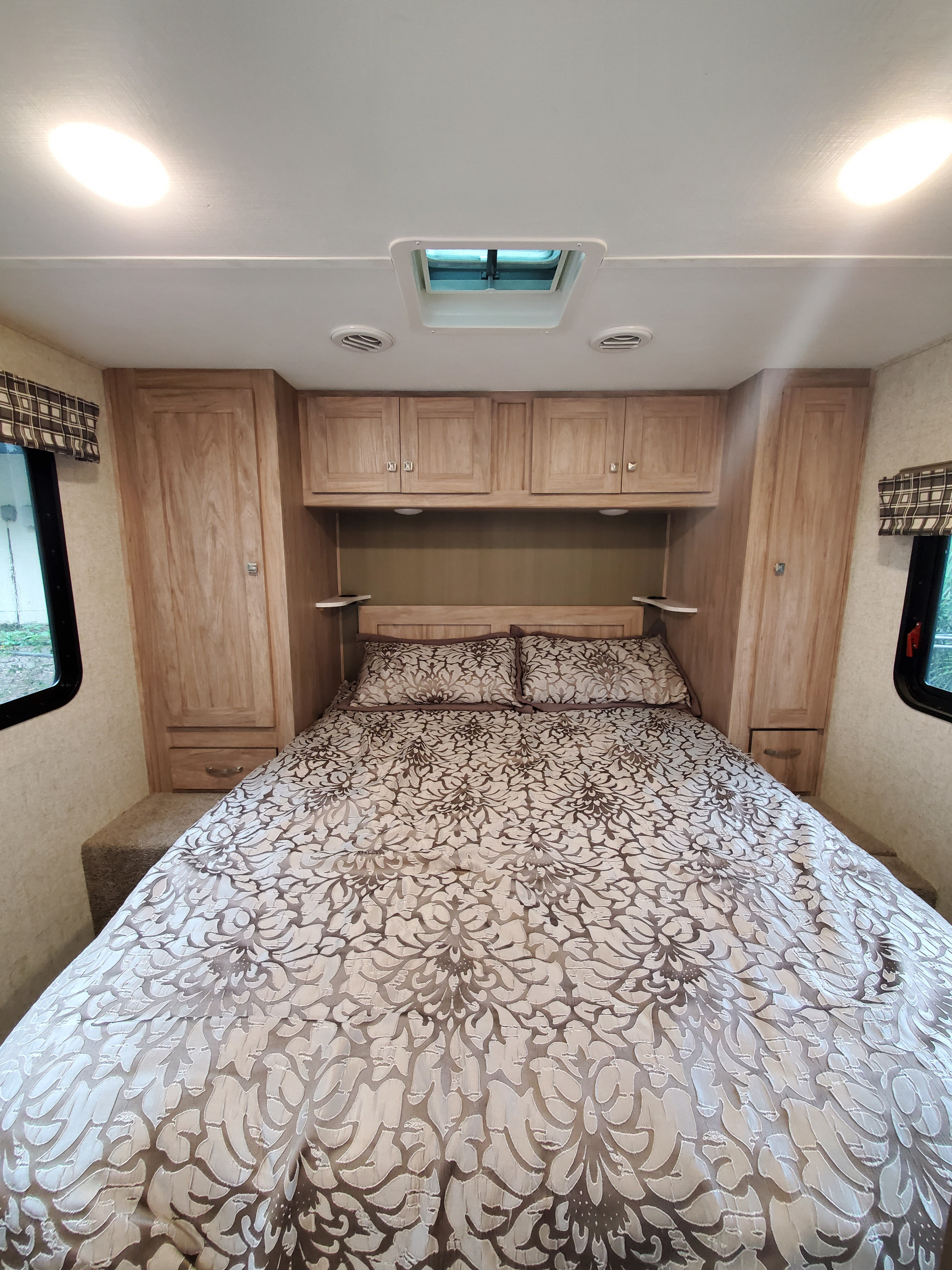 Compact RV rental bedroom featuring a queen bed with patterned bedding, light wood cabinetry, and ample storage.. Forest River Sunseeker 2019