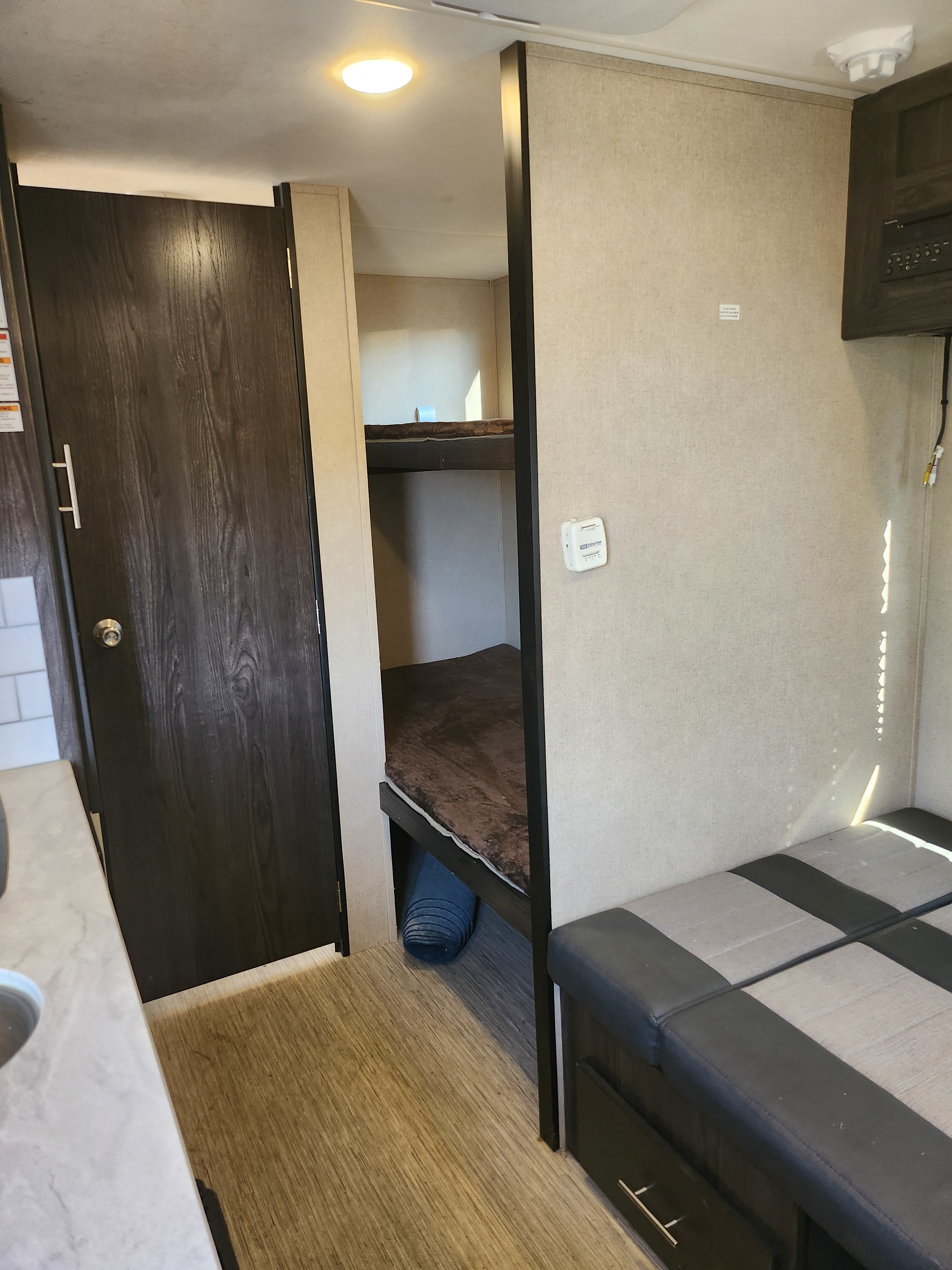 Cozy RV rental interior featuring a dark door, bunk beds, a comfy dinette seating area, and bright sunbeams.. Dutchmen Kodiak Cub 2018