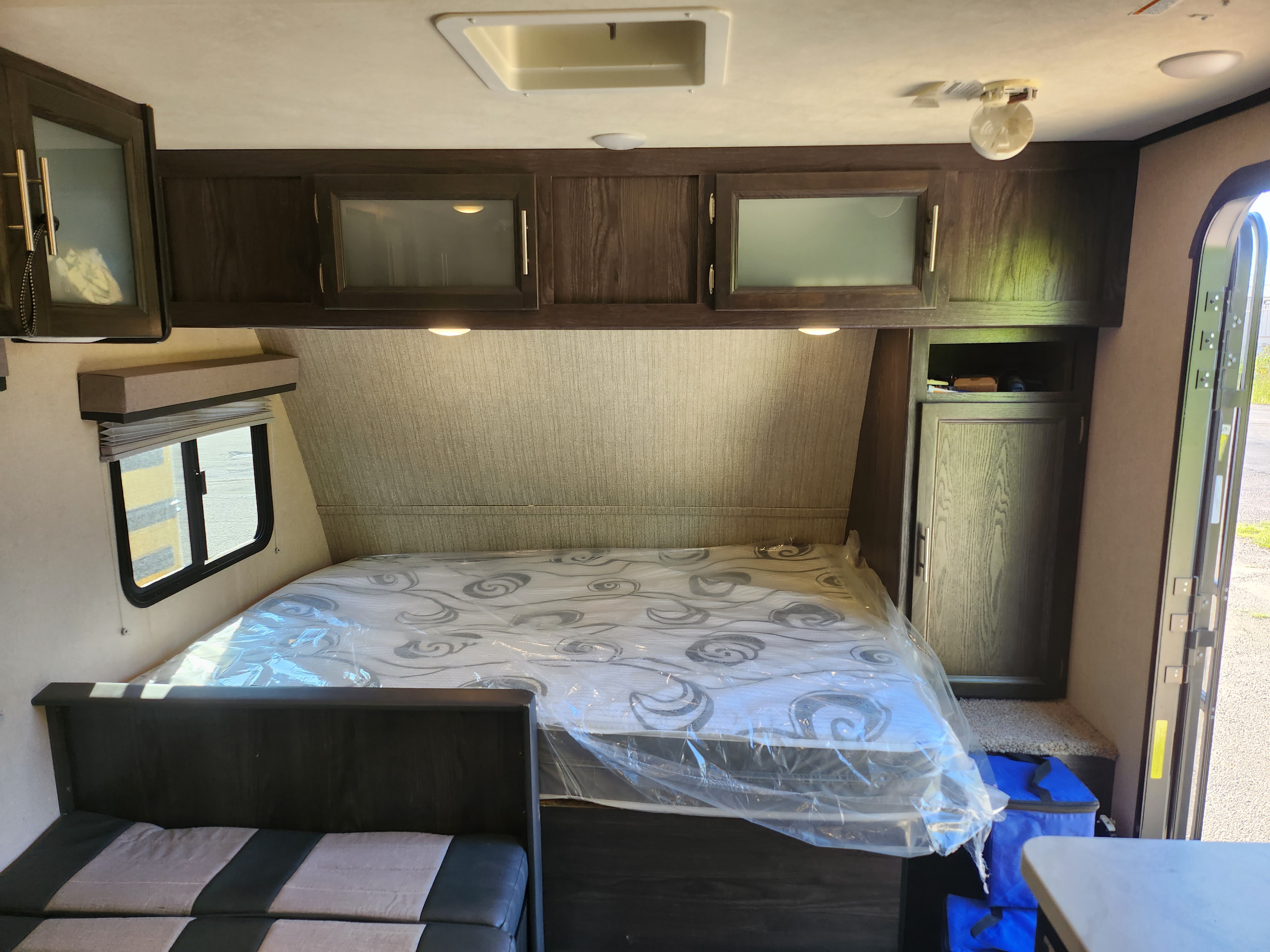 Bright RV rental bedroom area with a protected mattress, overhead cabinets, a window, and adjacent sofa seating.. Dutchmen Kodiak Cub 2018