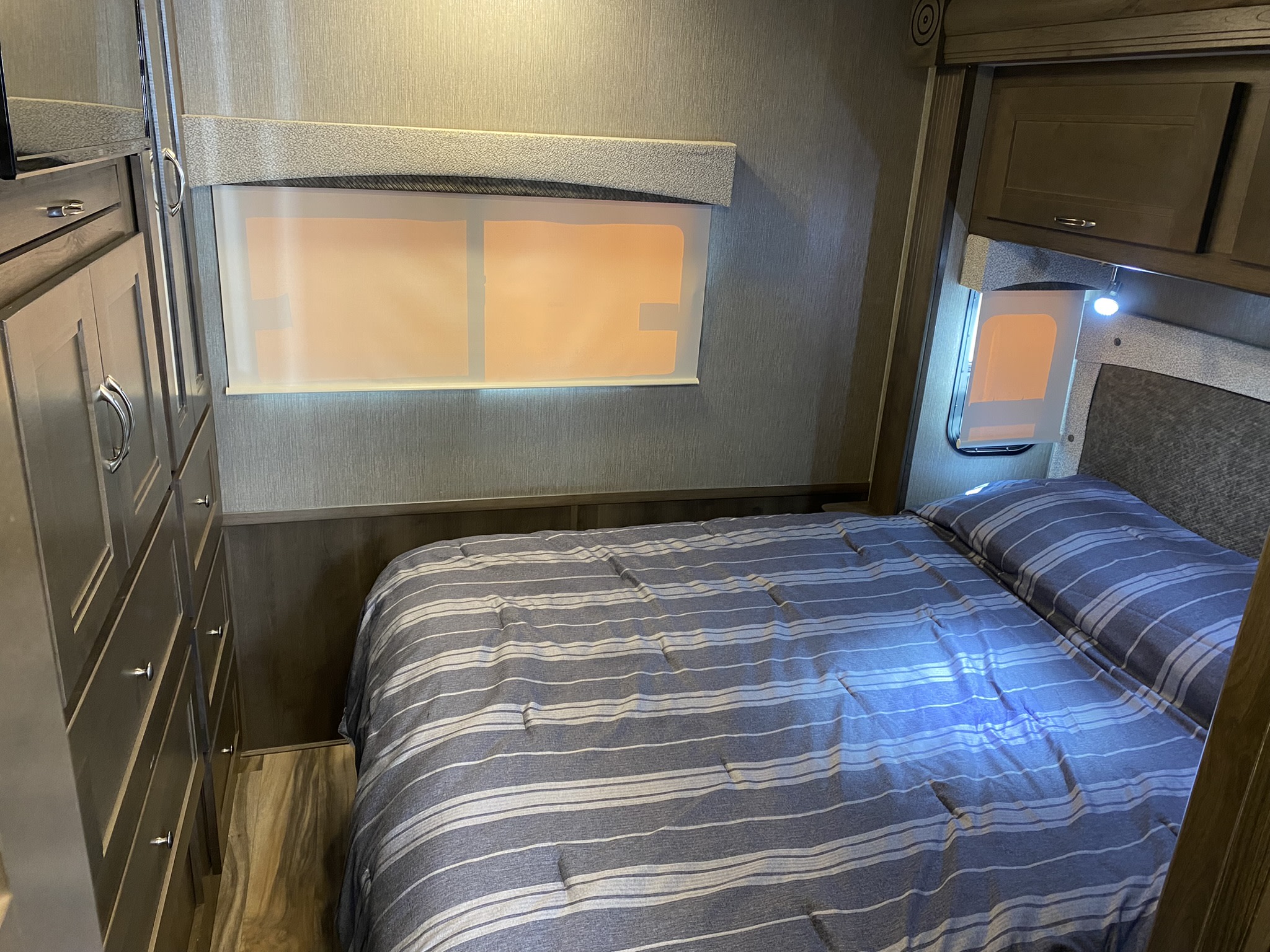 Cozy RV rental bedroom featuring a striped bed, built-in wardrobe, and window, ideal for mobile travel.. Nexus Wraith 2021