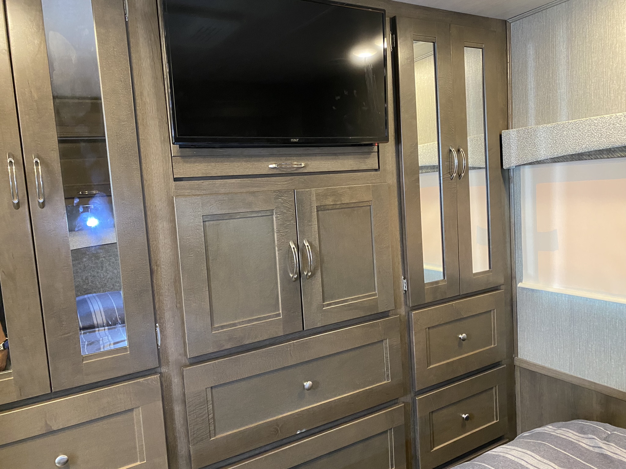 Dark wood cabinetry, TV, and mirrored storage in this RV rental bedroom.. Nexus Wraith 2021