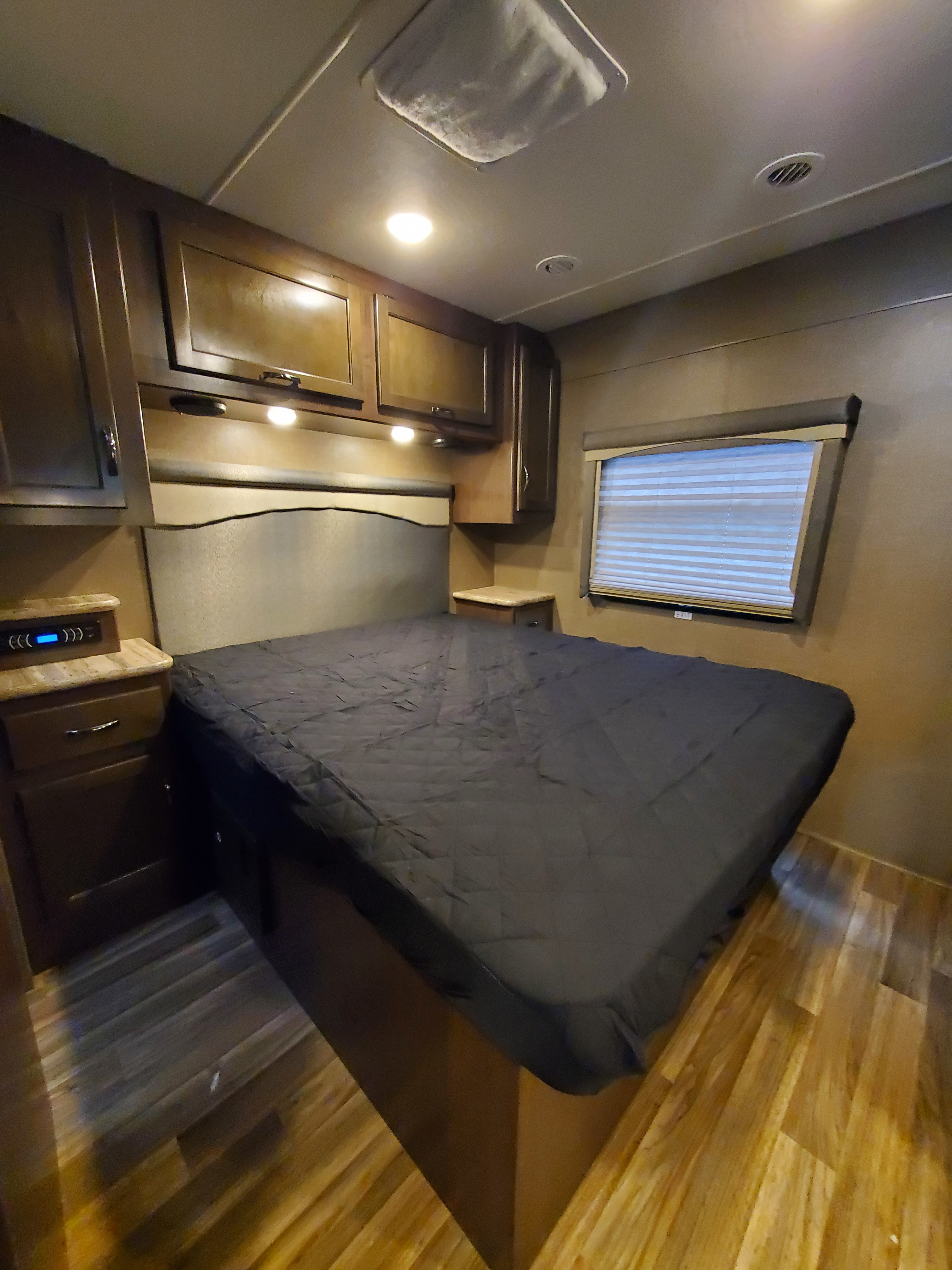 Experience comfort in this RV rental bedroom: complete with a bed, wood cabinets, and a window with blinds.. Thor Motor Coach A.C.E 2018