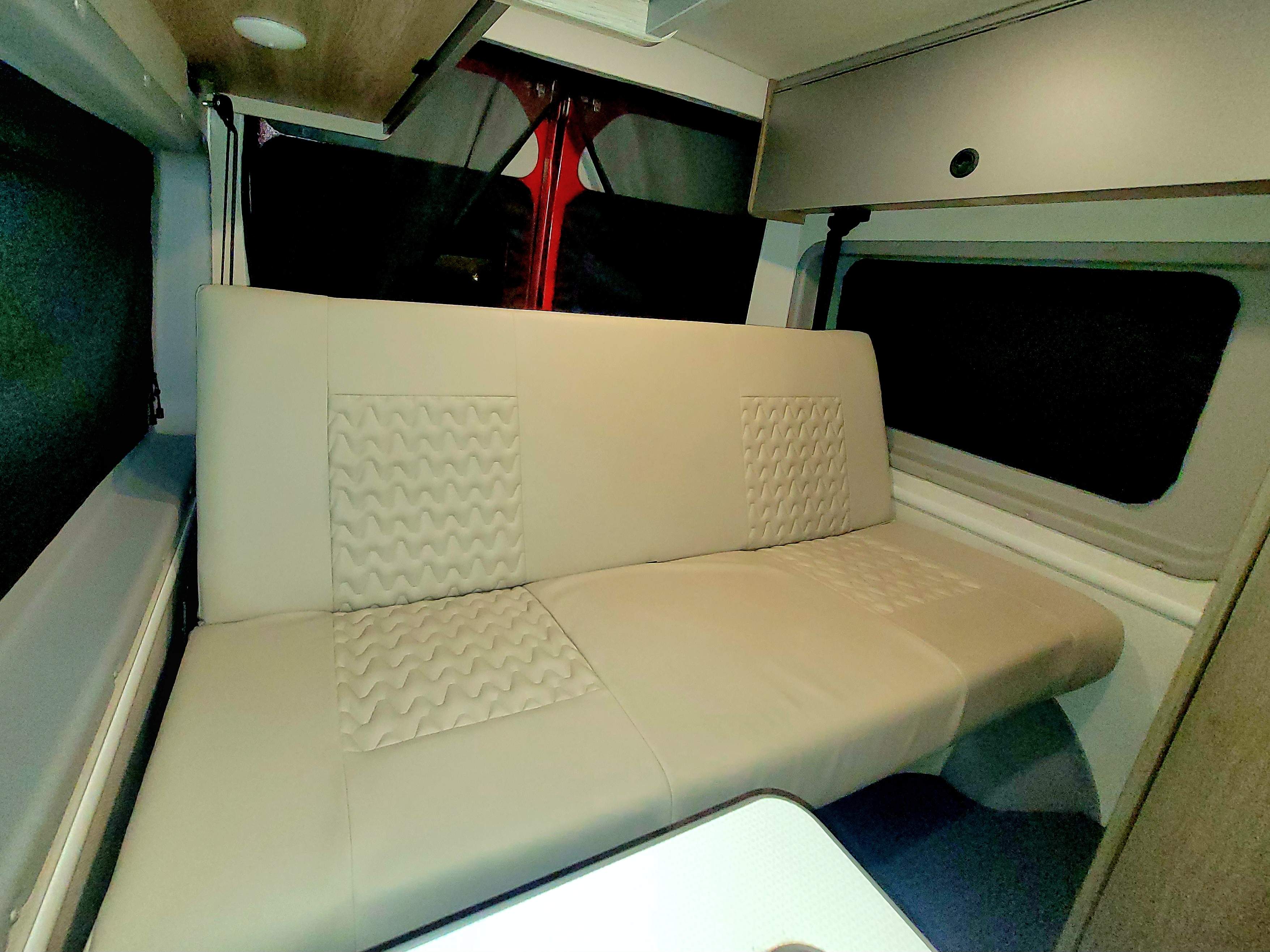Comfortable RV rental interior with spacious bench seating, overhead storage, and a small table, perfect for travel.. Winnebago Solis 2022