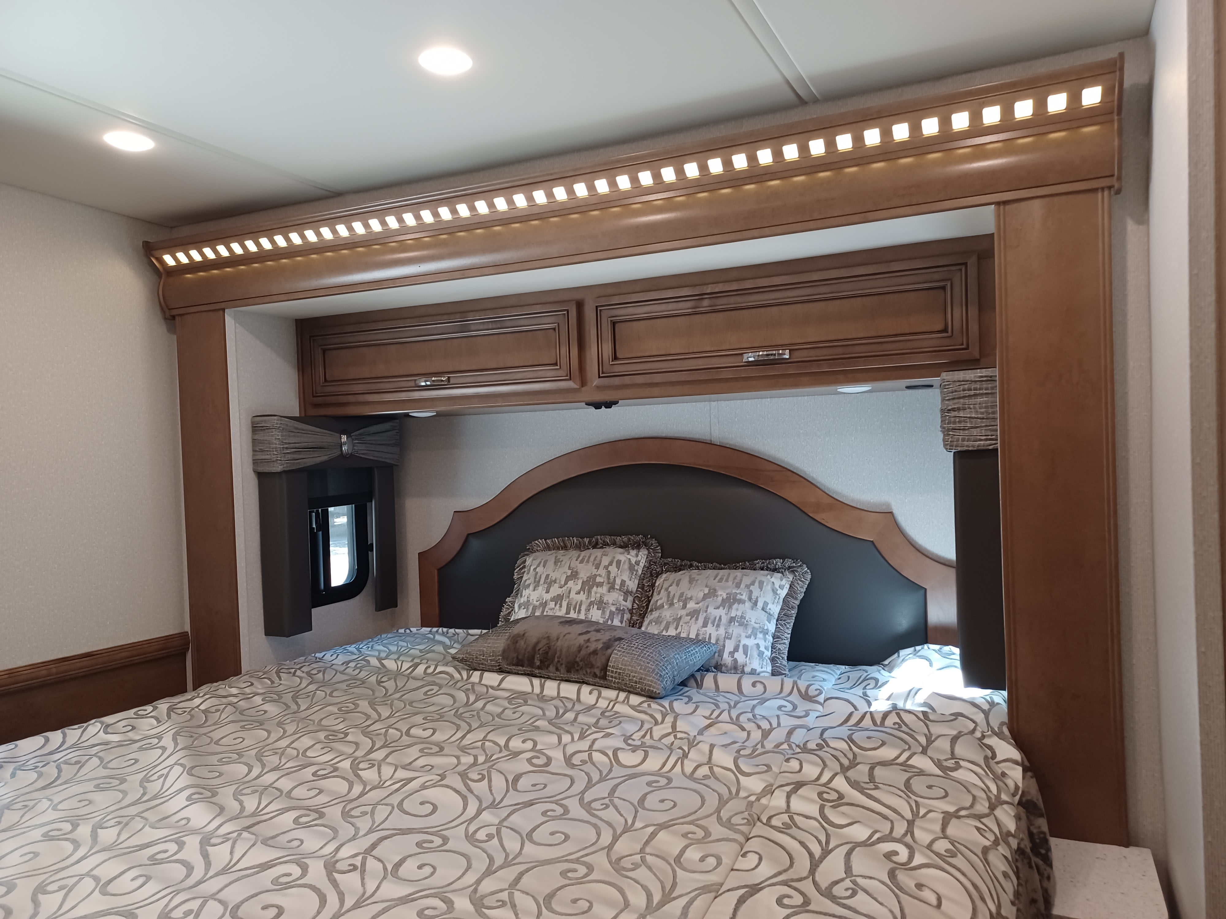 Comfortable RV rental bedroom with stylish bedding, wood headboard, overhead storage, and ambient lighting.. Newmar Bay star 2022