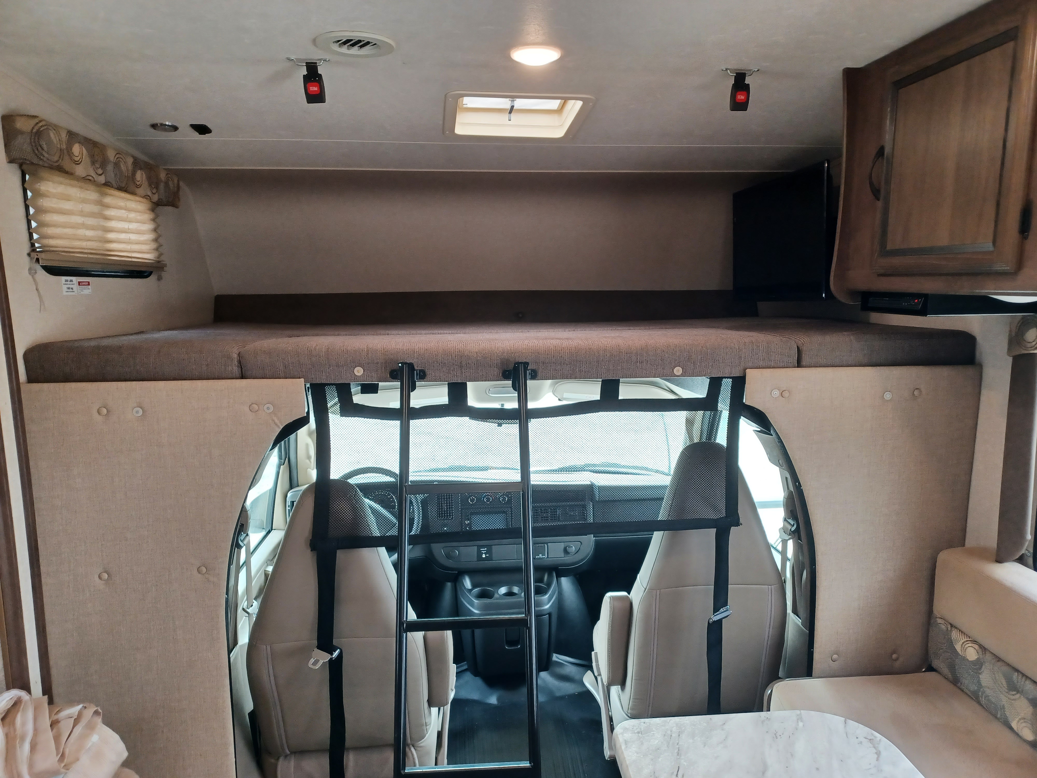 Inside your RV rental: view of the cab-over bunk with ladder, safety netting, and the spacious front cockpit with driver/passenger seats.. Coachmen Freelander 2019