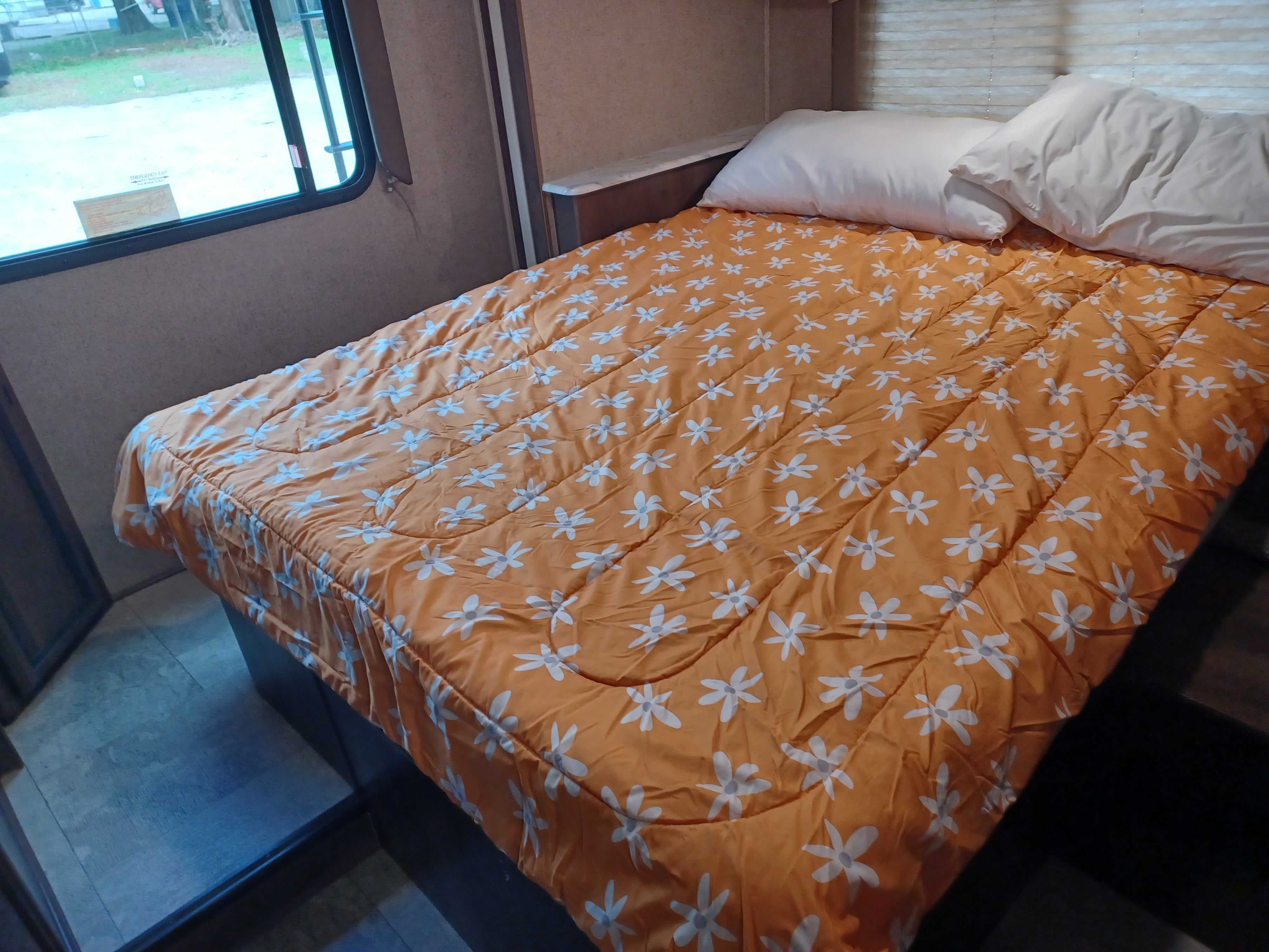 Cozy RV rental bedroom with a cheerful orange floral comforter and white pillows, ready for your next adventure.. Coachmen Freelander 2019
