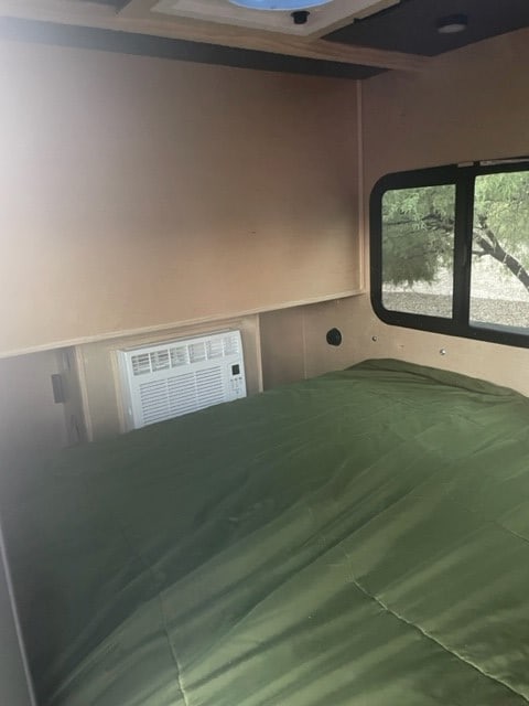 Inside this RV rental, find a cozy bedroom with a green bed, integrated AC unit, and window for comfortable travel.. Outbound Trailers T-REX 2023