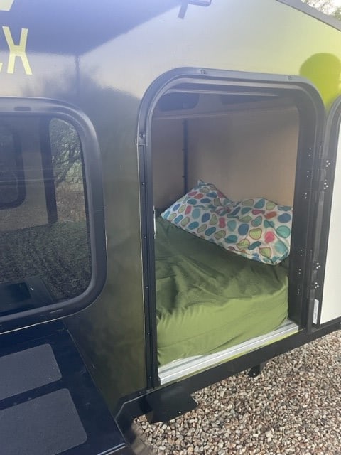 Image shows a compact RV rental's cozy sleeping area with mattress and pillow, ready for travel.. Outbound Trailers T-REX 2023