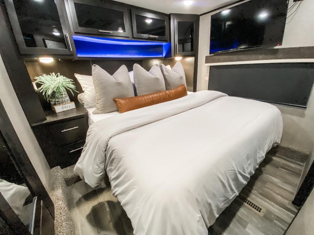 Discover a cozy, modern RV rental bedroom featuring a large bed, ambient blue lights, storage, and TV.. Jayco Seismic Toy Hauler 2021