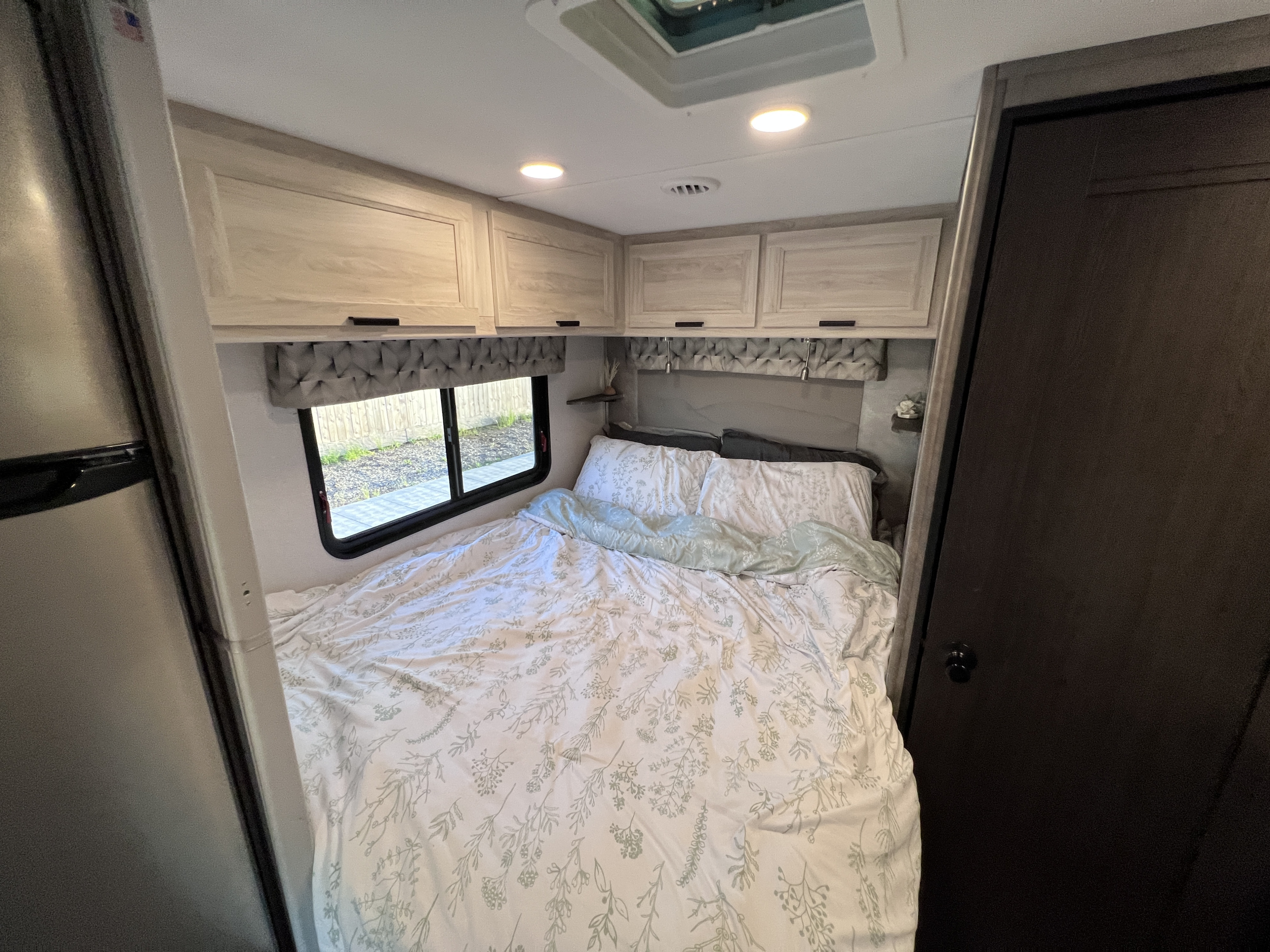 Cozy RV rental bedroom featuring a bed with patterned sheets, overhead storage, and a window view for a comfortable stay.. Forest River Sunseeker LE 2022