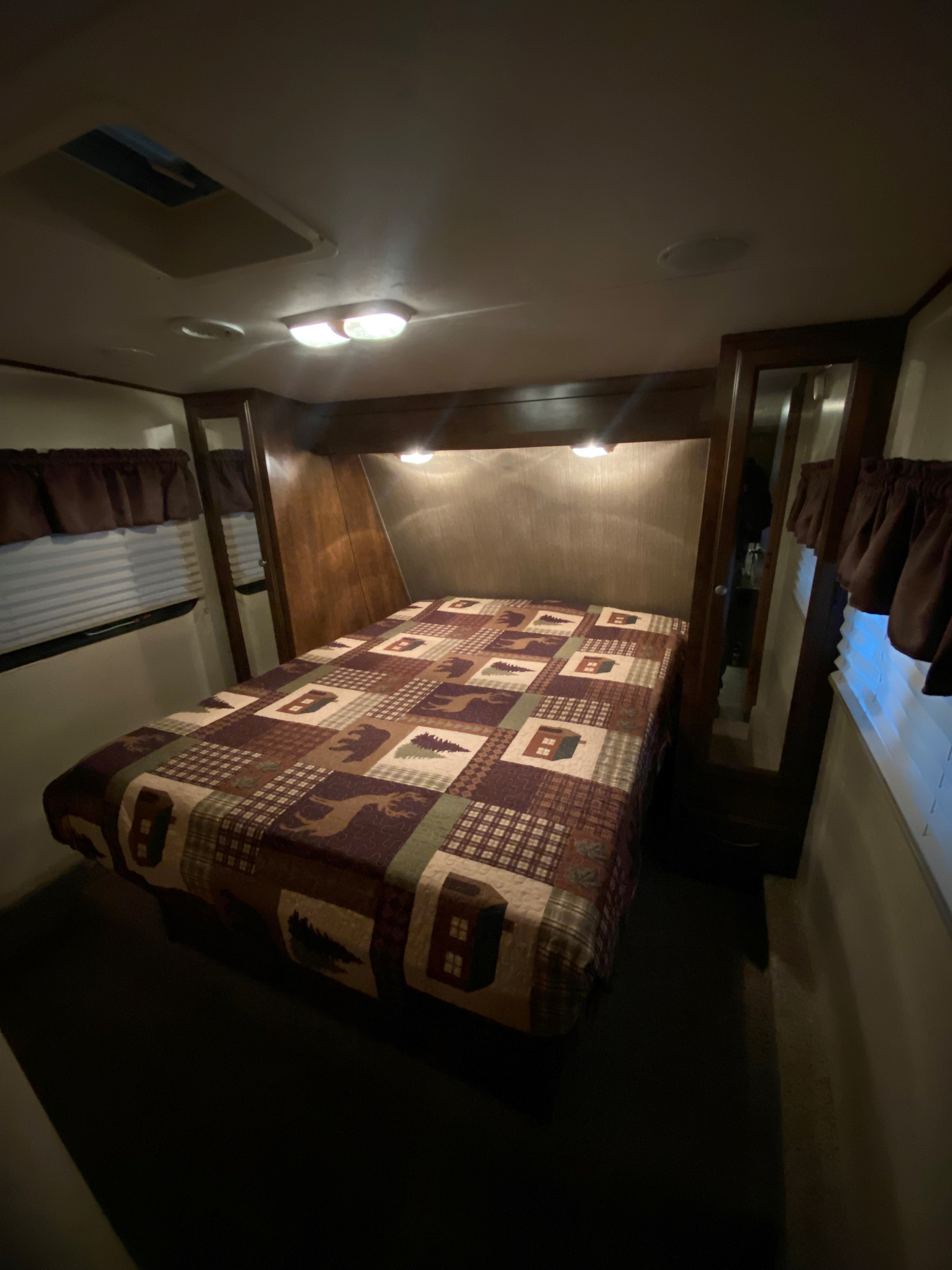 Cozy RV rental bedroom featuring a patterned comforter, reading lights, windows, and warm wood accents.. Coachman Chaparral 2014