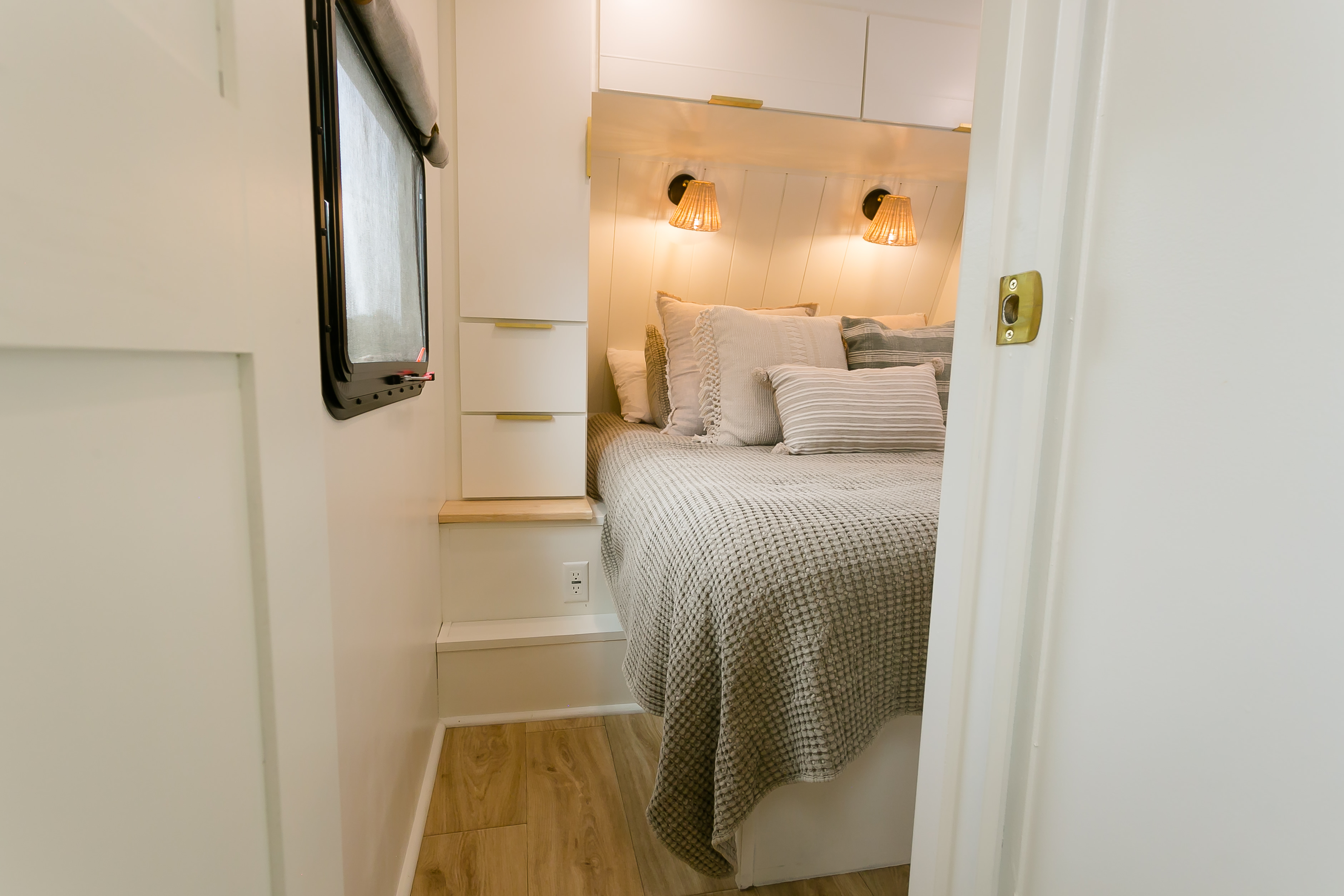 Cozy RV rental bedroom featuring a bed with textured bedding, warm sconce lights, and compact built-in storage.. Grand Design Imagine 3250BH 2021