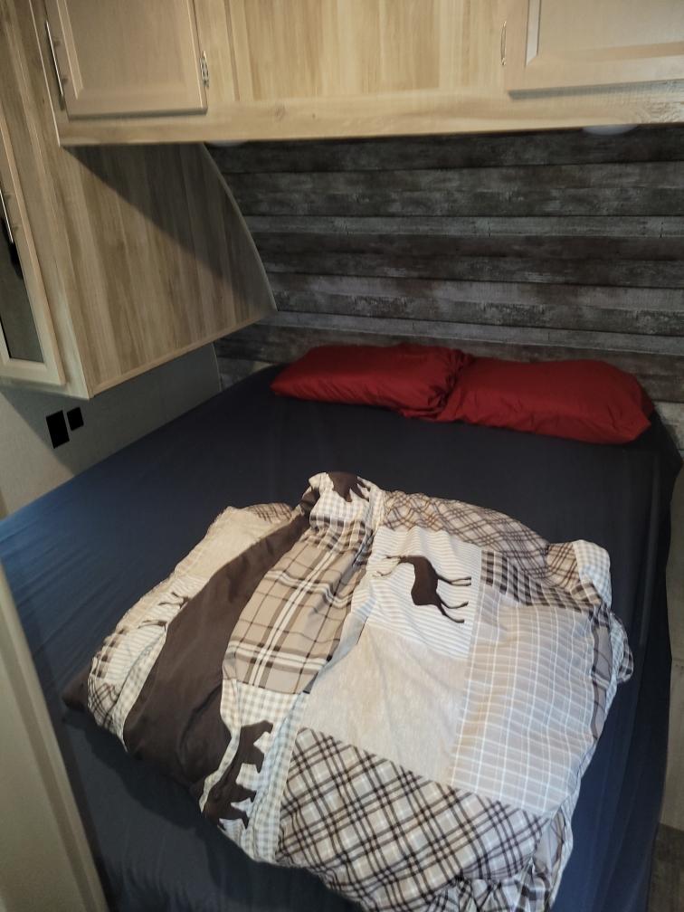 Cozy RV rental bedroom with rustic wood wall, red pillows, and wildlife-themed comforter. Compact and inviting.. Coachmen 323BHDSCK 2021