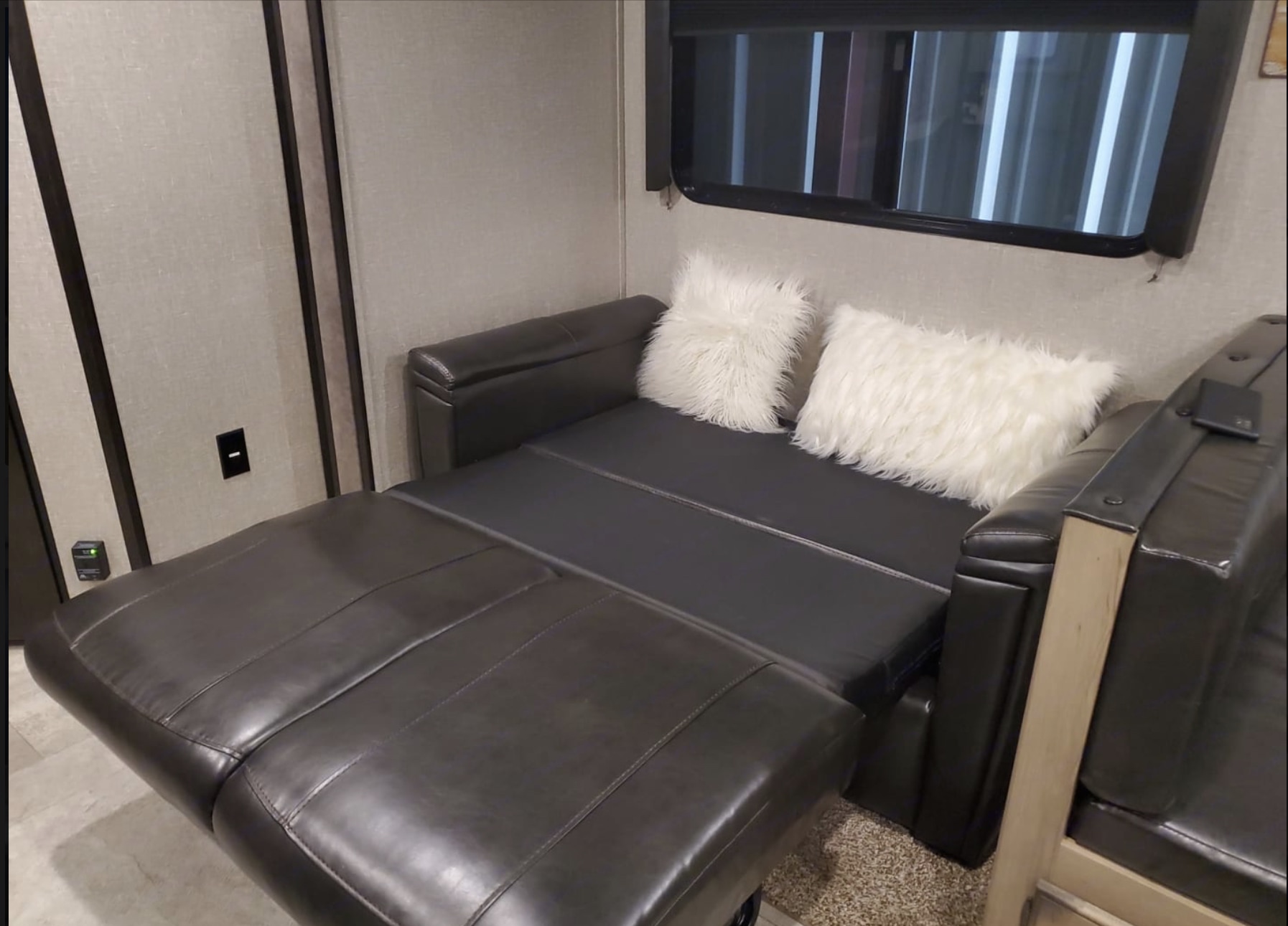 RV rental featuring a black leather sofa converting into a bed, adorned with two fluffy white pillows.. Heartland RVs Mallard 2020