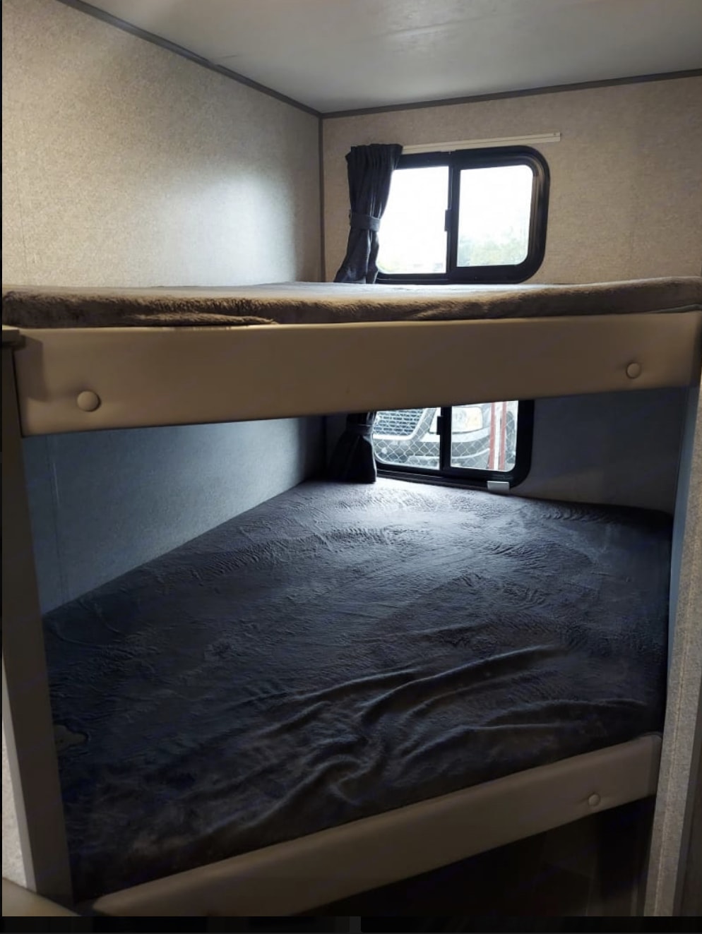 Inside an RV rental, two bunk beds with grey bedding provide comfortable sleeping, each featuring a window.. Heartland RVs Mallard 2020