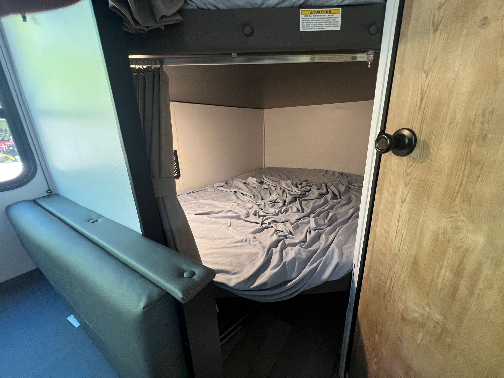 RV rental's compact interior features a gray elevated bunk bed, bench, and wooden door for cozy travel.. Keystone RV Springdale 2022