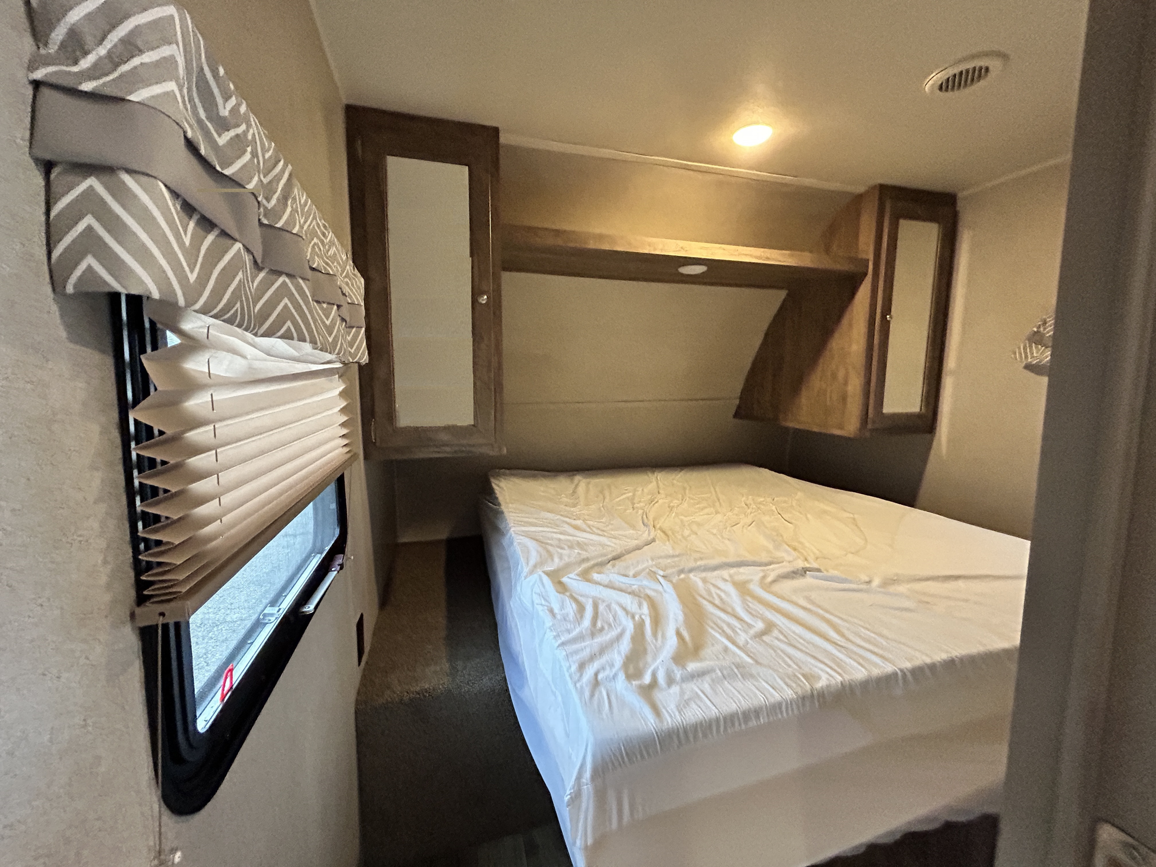 RV rental bedroom interior: a compact space with white-covered bed, overhead storage, and a window with pleated blinds.. Forest River Puma 2018