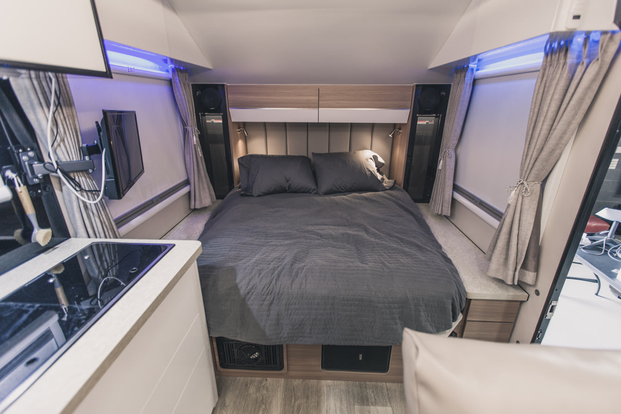 Inside a modern RV rental: a spacious gray bed, compact kitchen with cooktop, wall-mounted TV, and blue ambient lighting. Cozy travel.. Black Series Black Series Trailer 2022