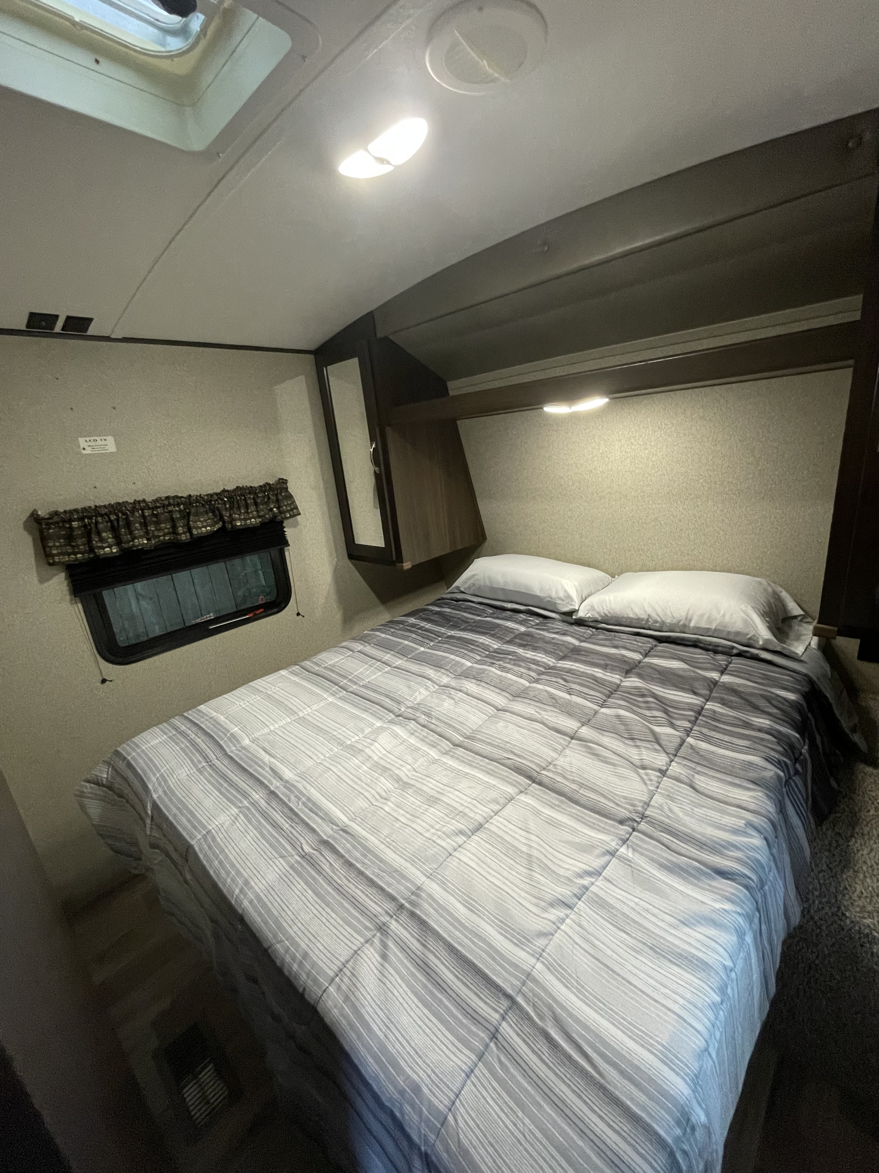 This cozy RV rental bedroom features a comfy striped bed, a window, and integrated lighting.. Keystone RV Springdale 2020
