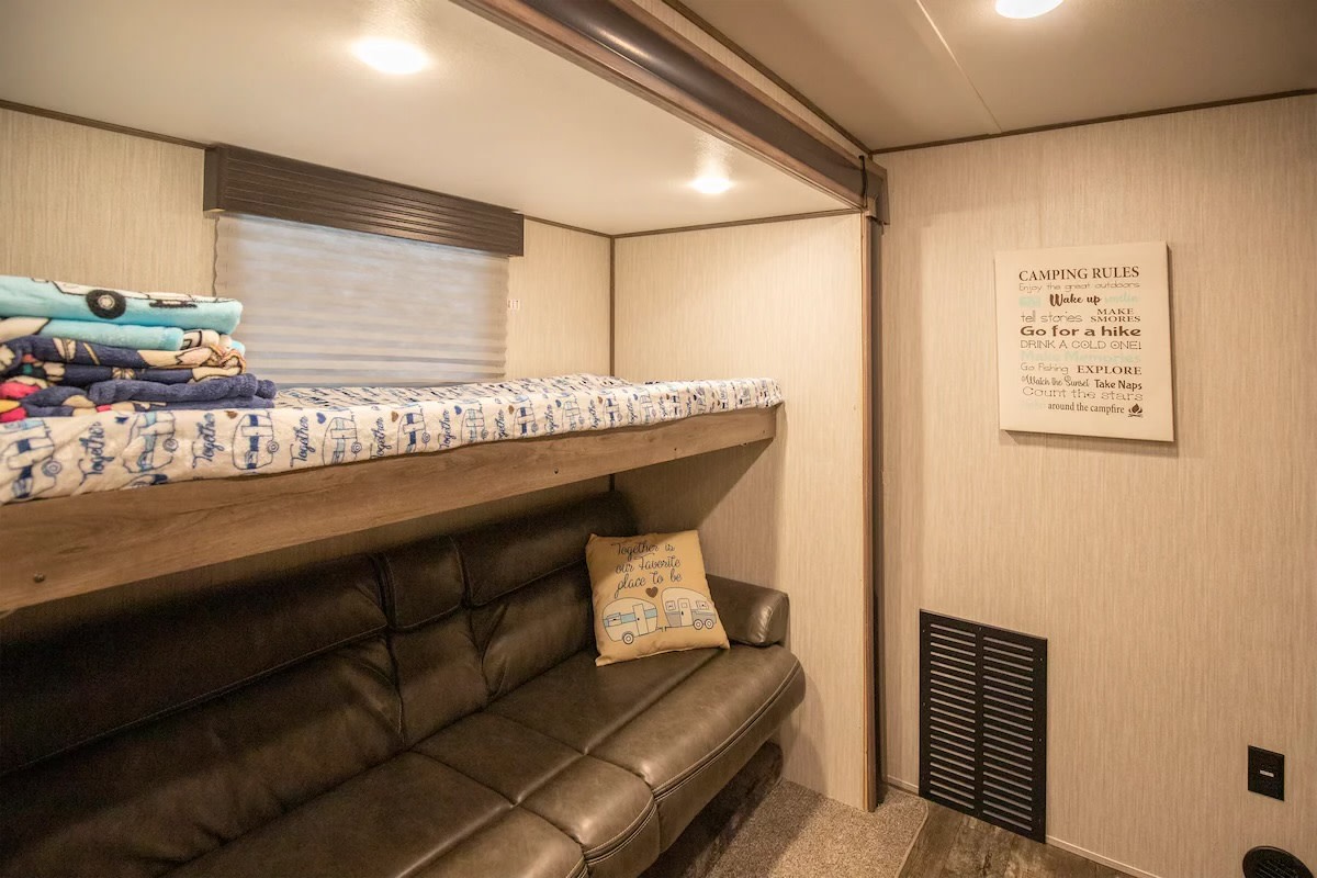 This RV rental features cozy bunk beds above a sofa, a window, and a "Camping Rules" sign, perfect for family adventures.. Forest River Sabre 2019