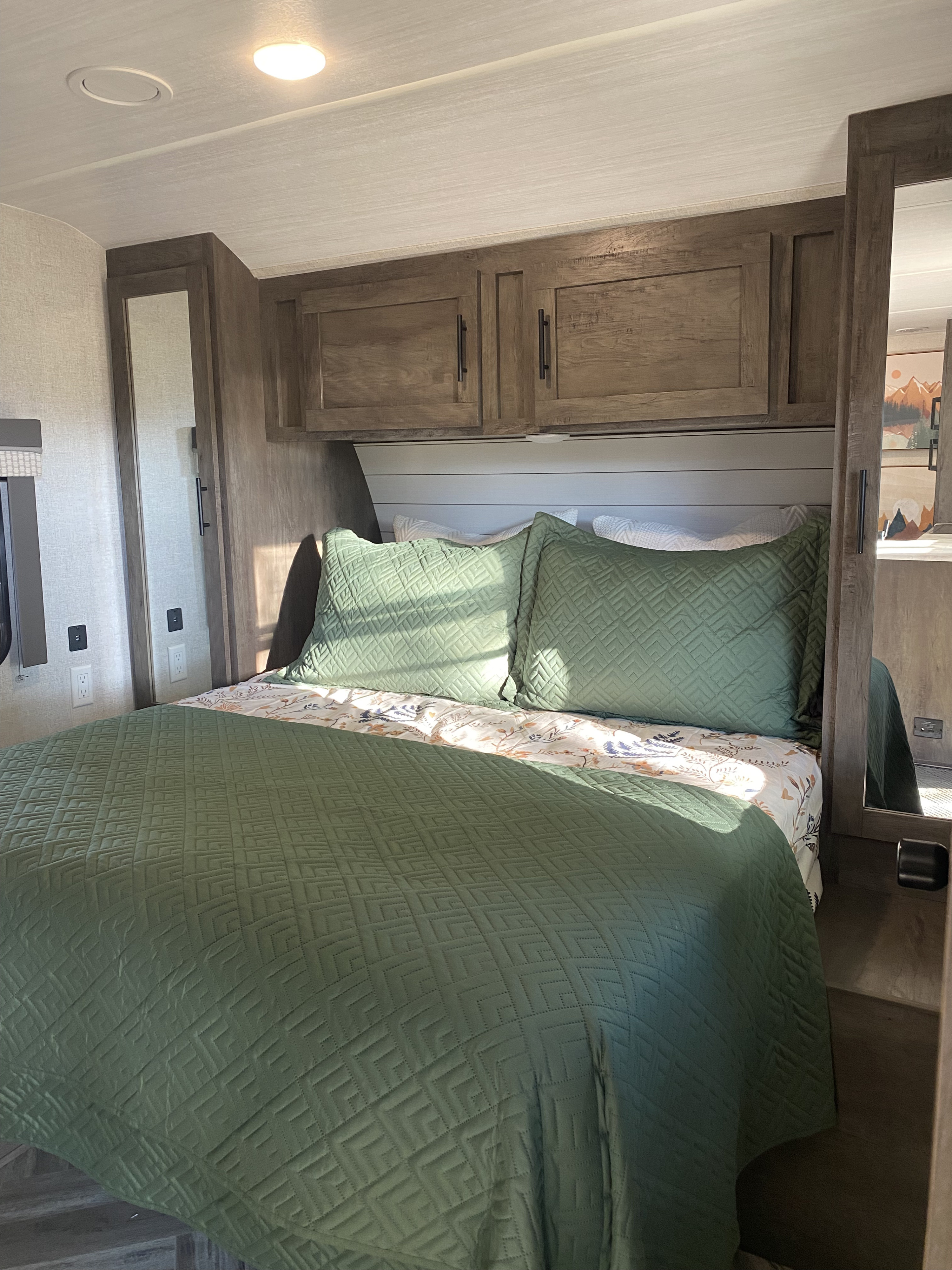 A comfortable RV rental bedroom interior features a green quilted bed, overhead storage, and mirrored closets for guests.. Forest River Salem 2021
