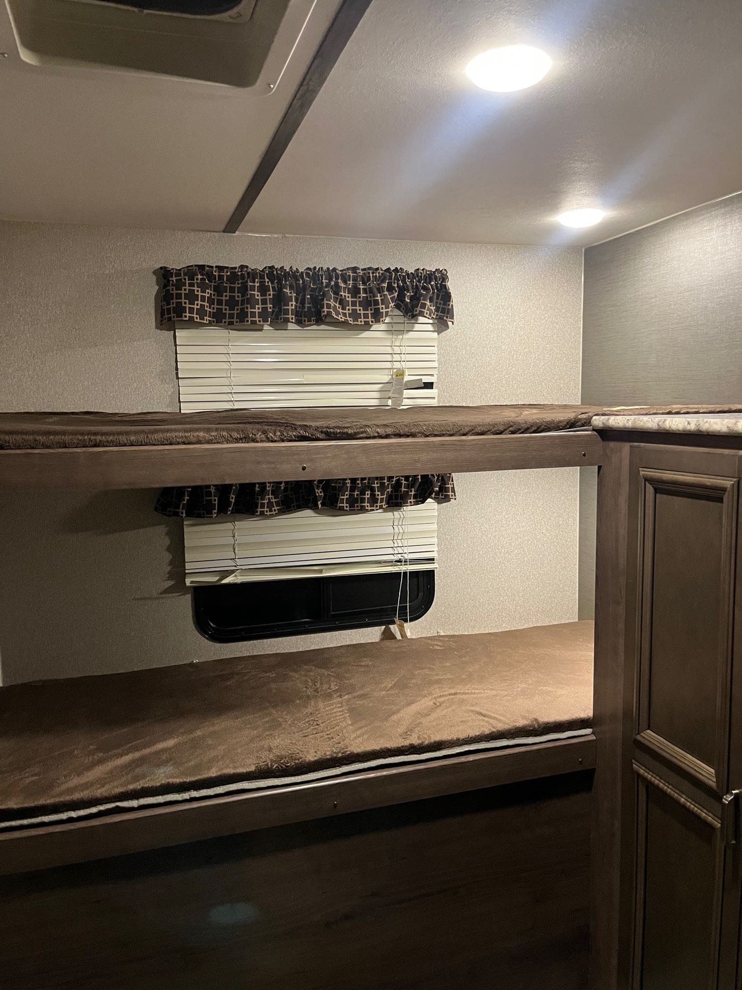 Cozy bunk beds in an RV rental, featuring brown bedding, window blinds, and bright overhead lights.. Keystone RV Passport Grand Touring 2019