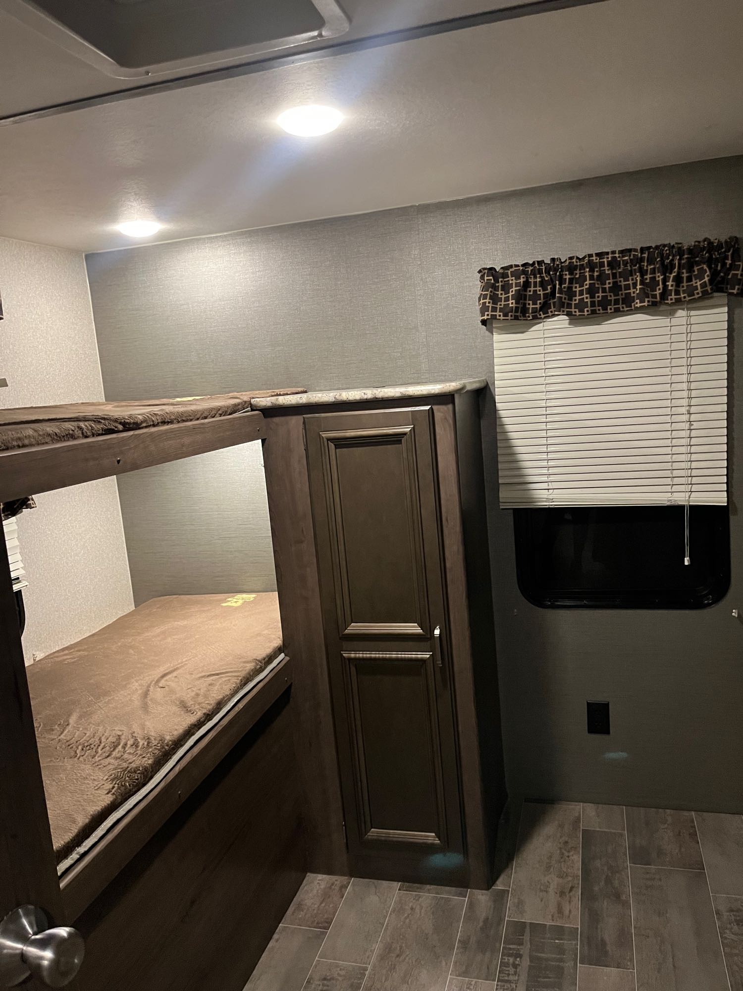This RV rental bunk bed area features two cozy bunks, a wooden wardrobe, and a window with blinds, all in a neutral decor.. Keystone RV Passport Grand Touring 2019