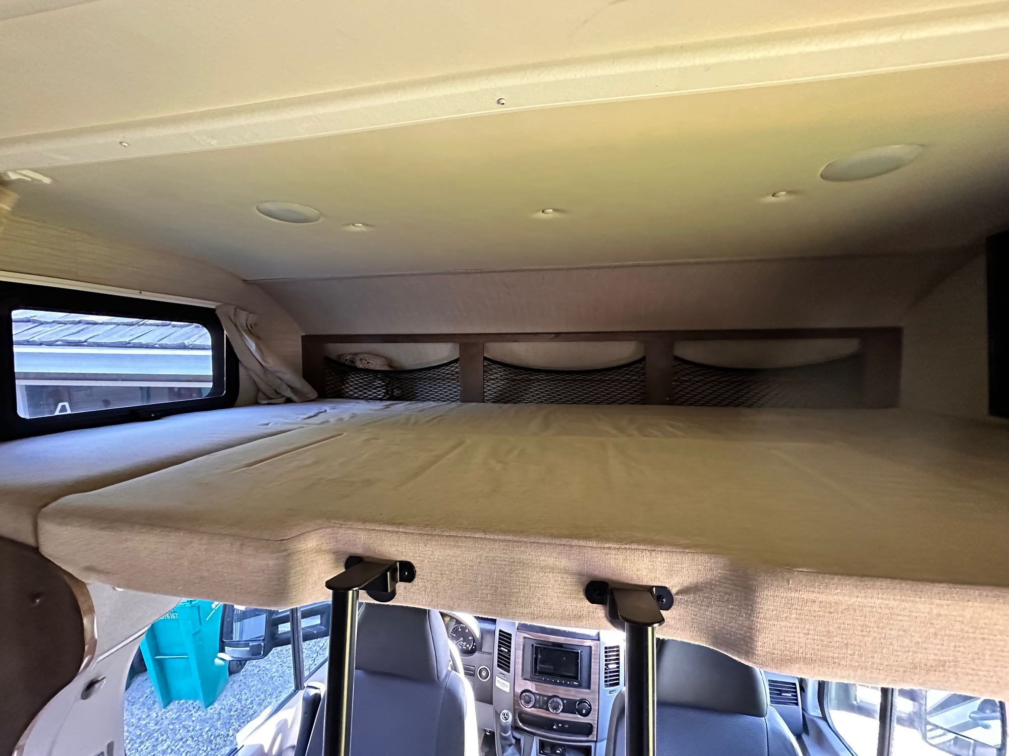 RV rental interior: cab-over bunk with mattress, bright overhead lights, storage nets, and front cockpit view.. Jayco Melbourne 2018