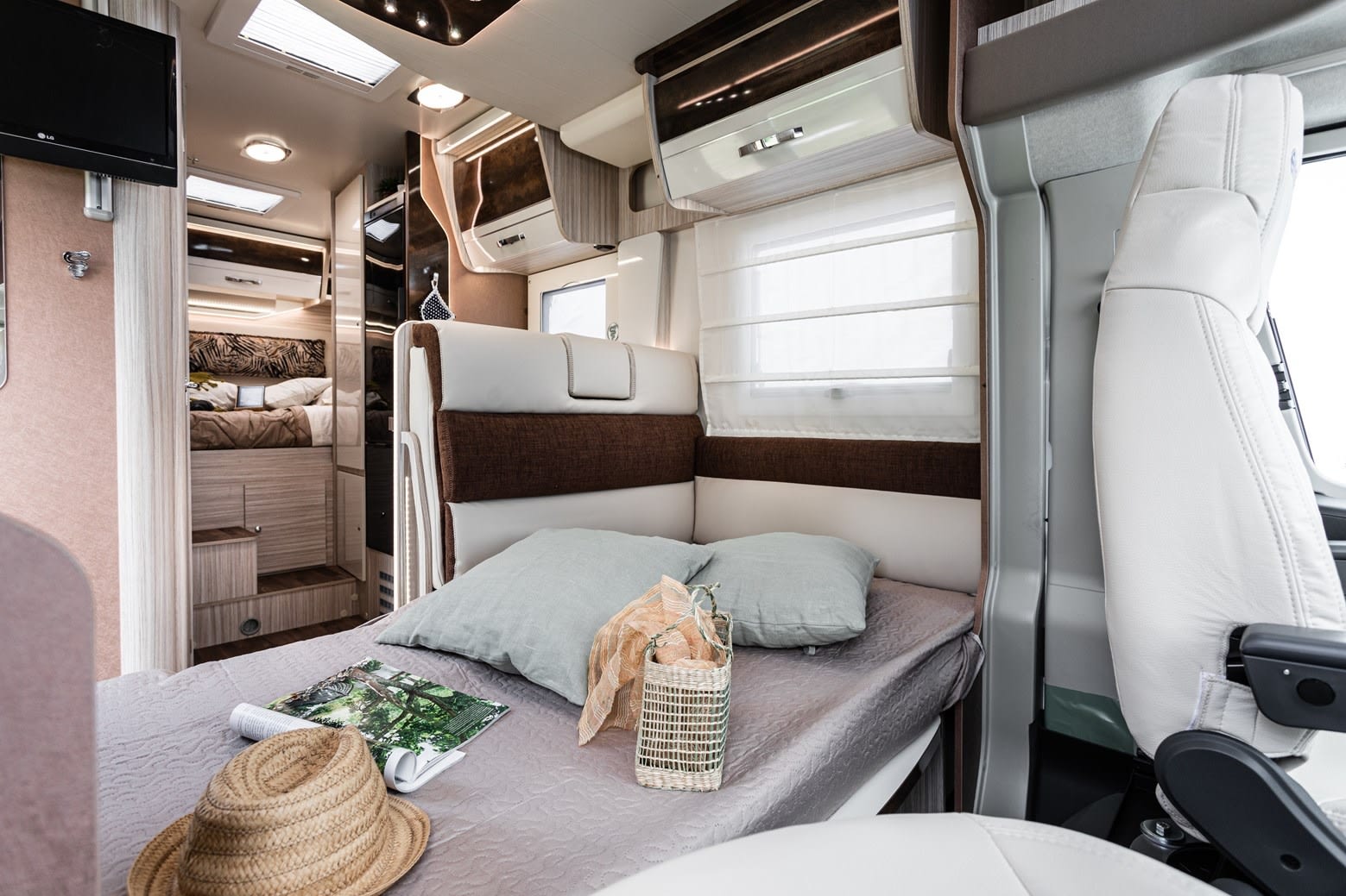 Cozy RV rental interior featuring a comfortable bed with light pillows, overhead storage, and driver's seat. Ideal for travel.. Elnagh 532 2023