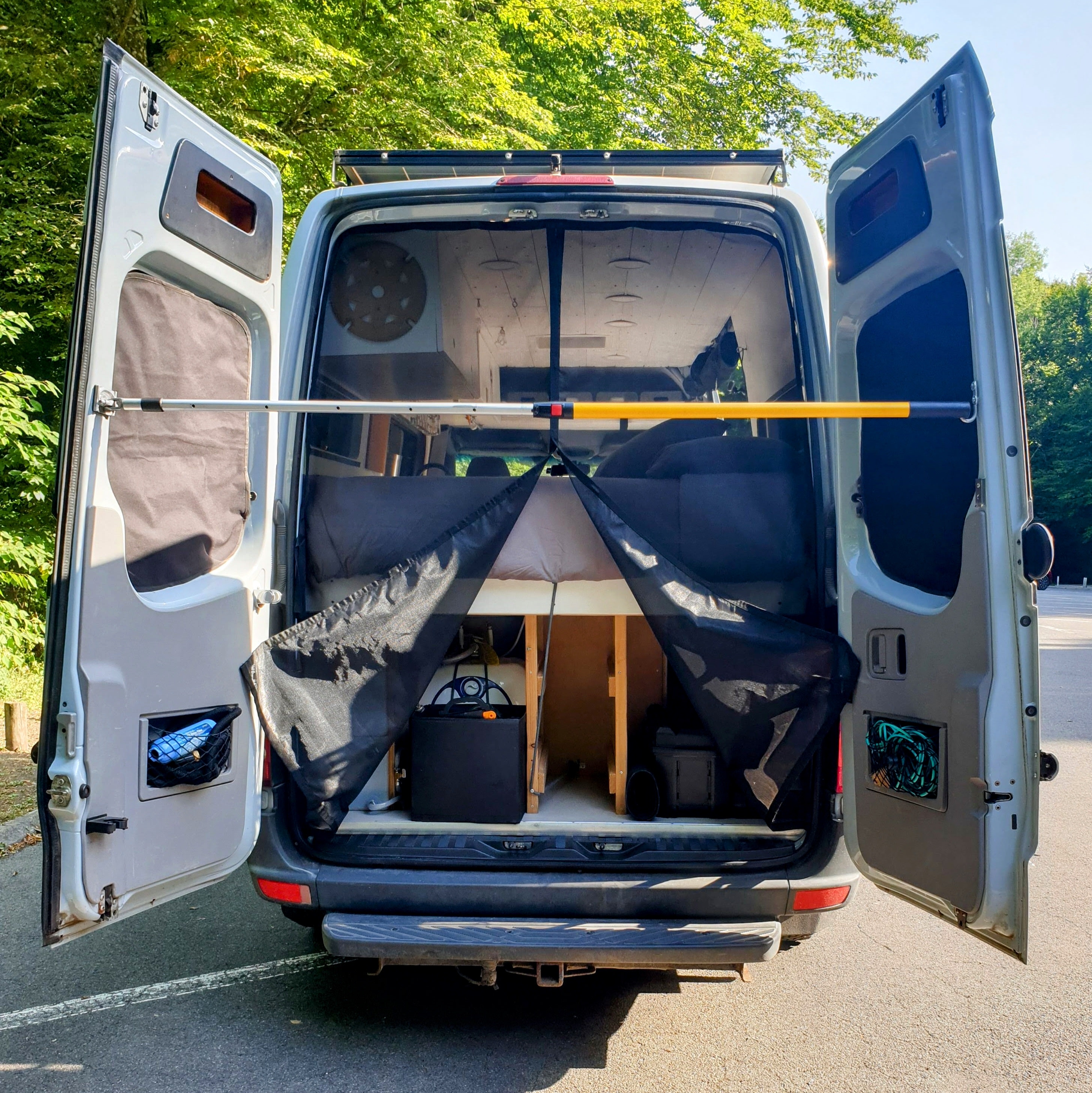 RV rental camper van, rear doors open wide. Inside, a comfortable bed, storage, and mesh screen for outdoor living.. Mercedes-Benz Sprinter 2012