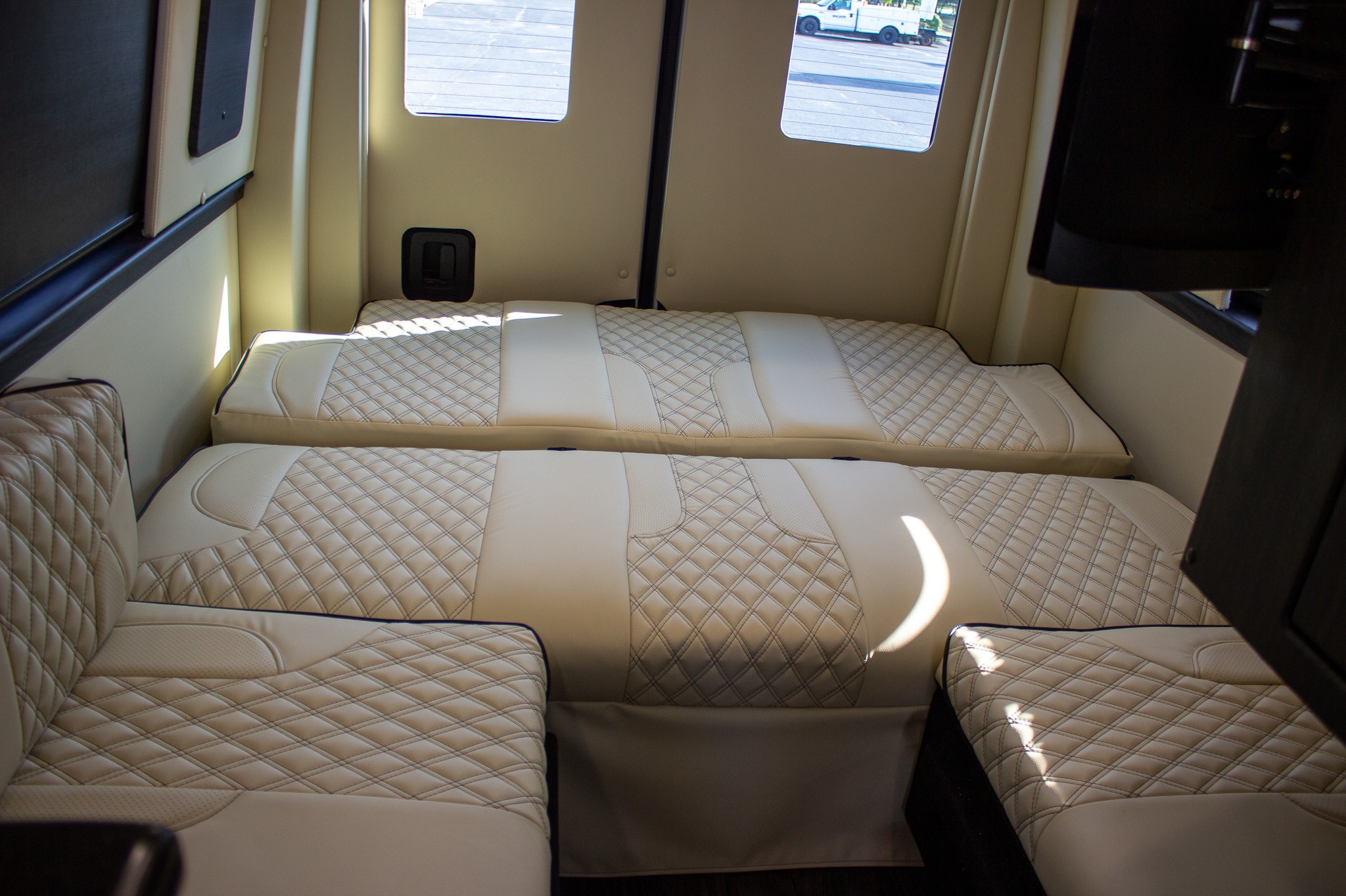 Cream quilted seating converts to beds inside this spacious RV rental, offering comfort and style.. Midwest Automotive Designs Ultimate CamperVan 2023