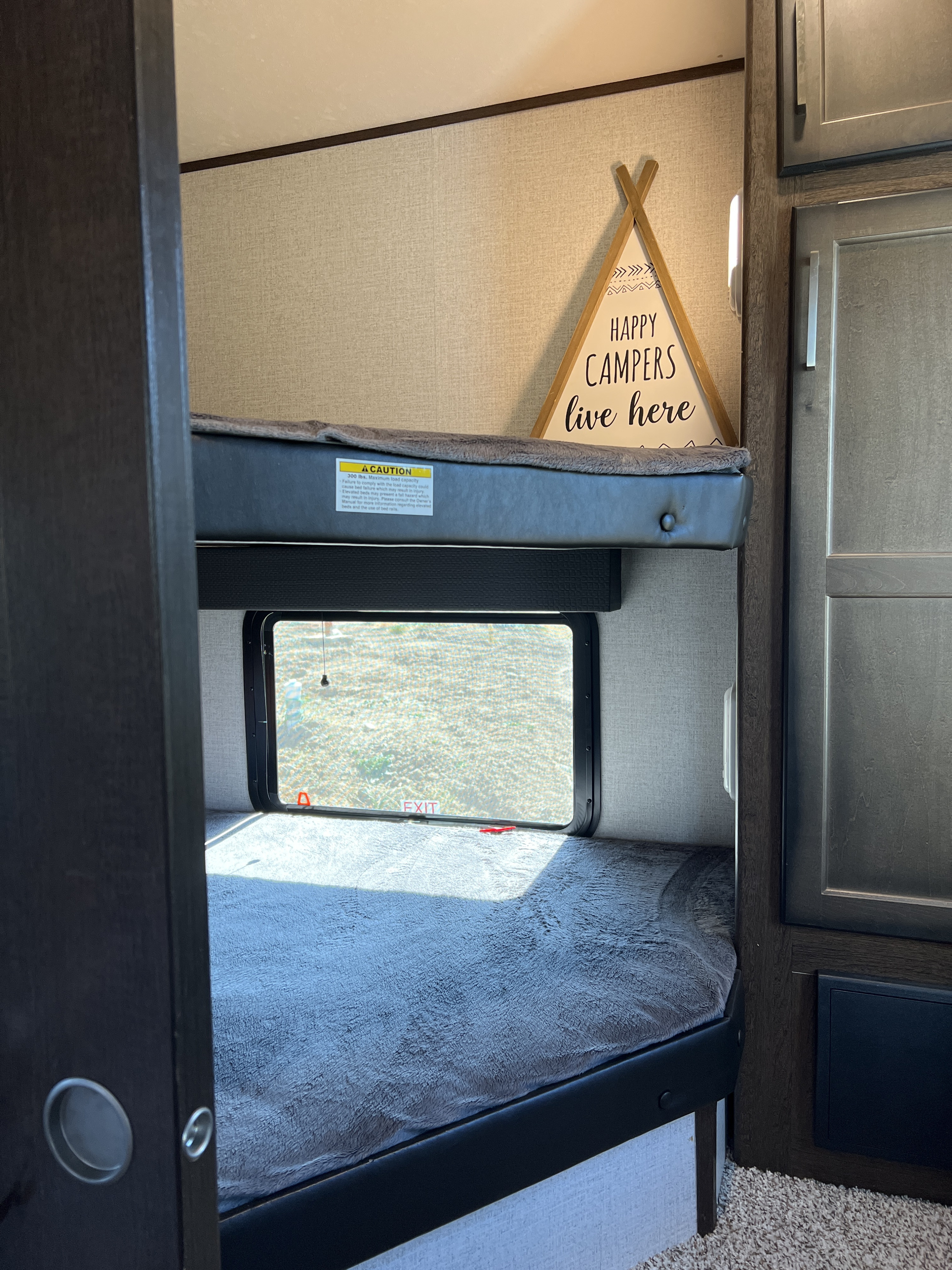 Cozy RV rental bunk beds, offering a comfortable sleeping area with a window view and "Happy Campers" sign.. Atlas Atlas Fifth Wheel 2020