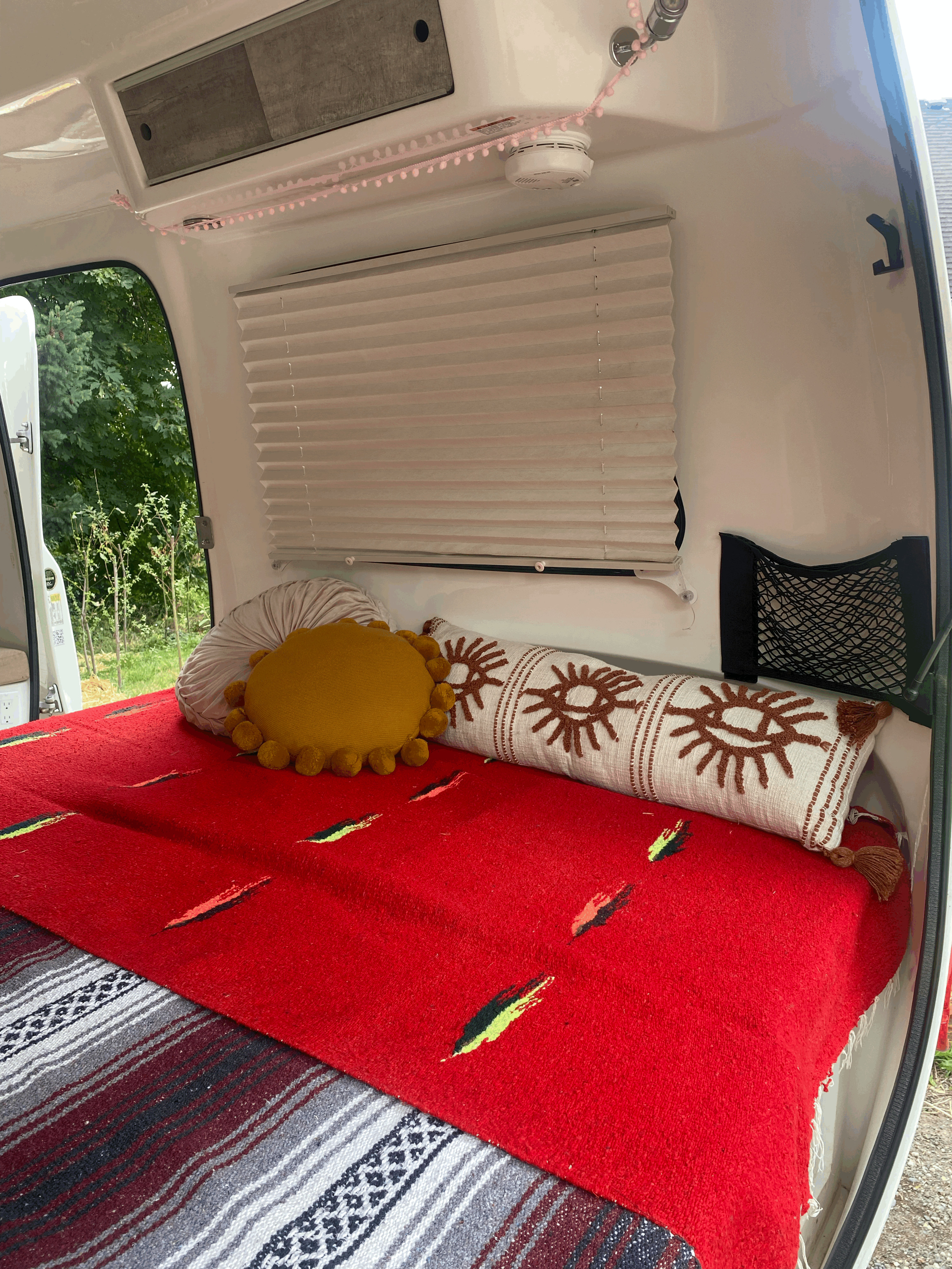 Stylish RV rental interior with a red blanket bed, sun-design pillow, and practical storage solutions.. Happier Camper HC1 2022