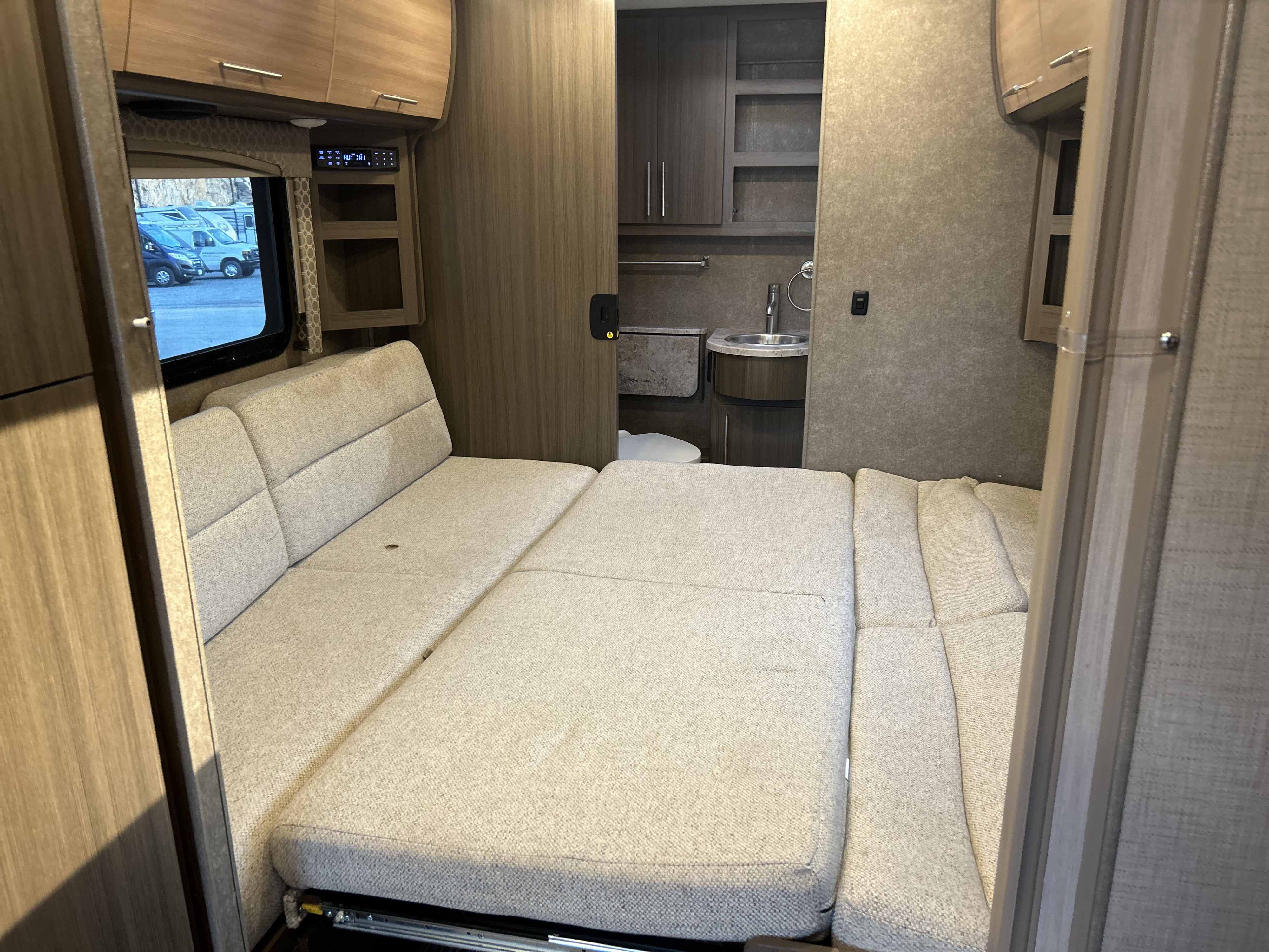 RV rental camper van interior featuring a light-colored convertible bed and compact rear bathroom.. Thor Axis 2018
