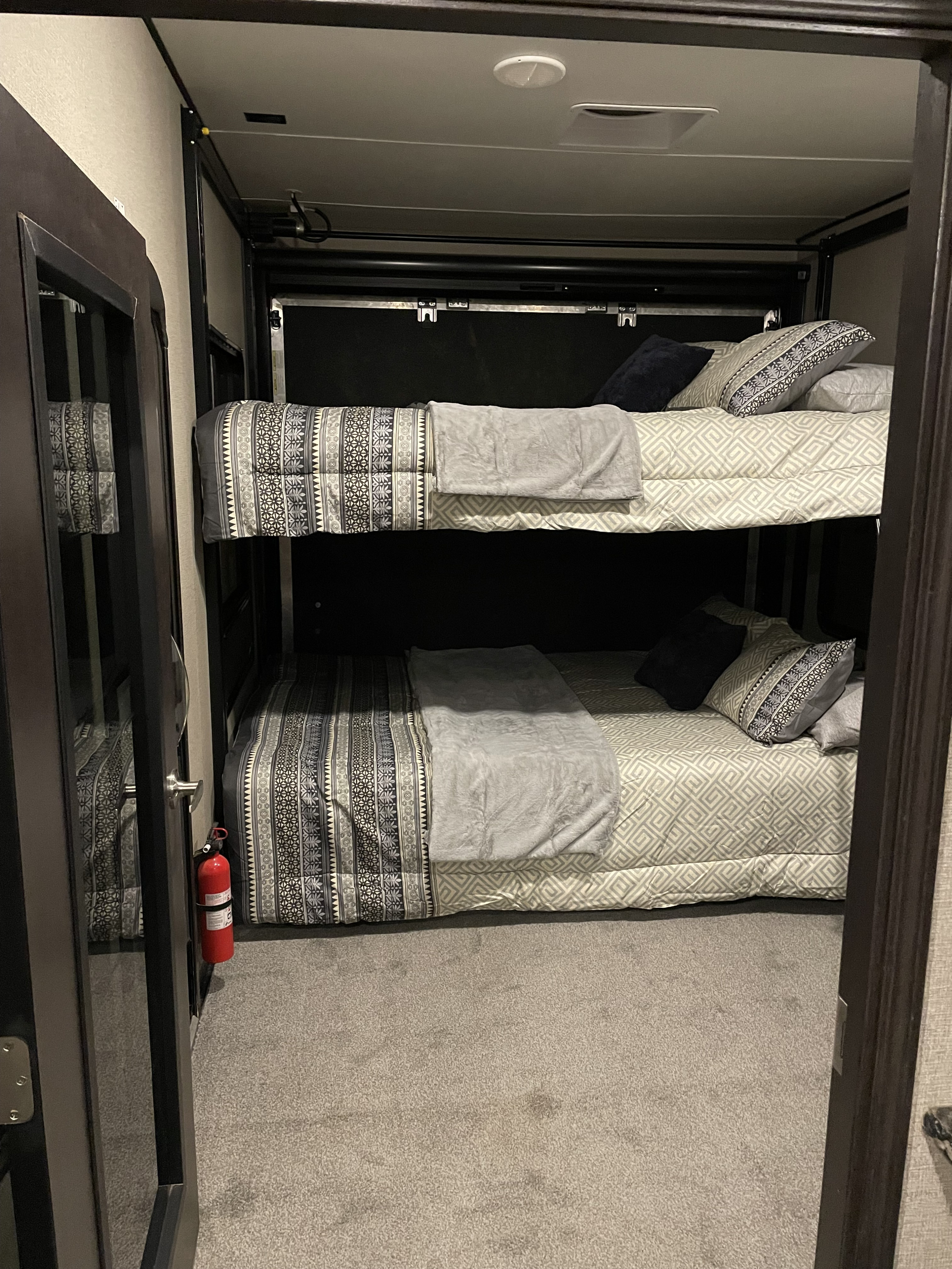 Comfortable bunk beds in an RV rental, featuring patterned bedding and a fire extinguisher for safety.. Keystone Carbon 2017